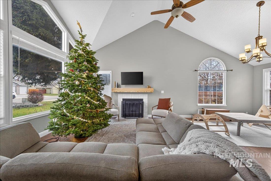 Living room with a tiled fireplace, wood finished floors, high vaulted ceiling, a ceiling fan, and a chandelier