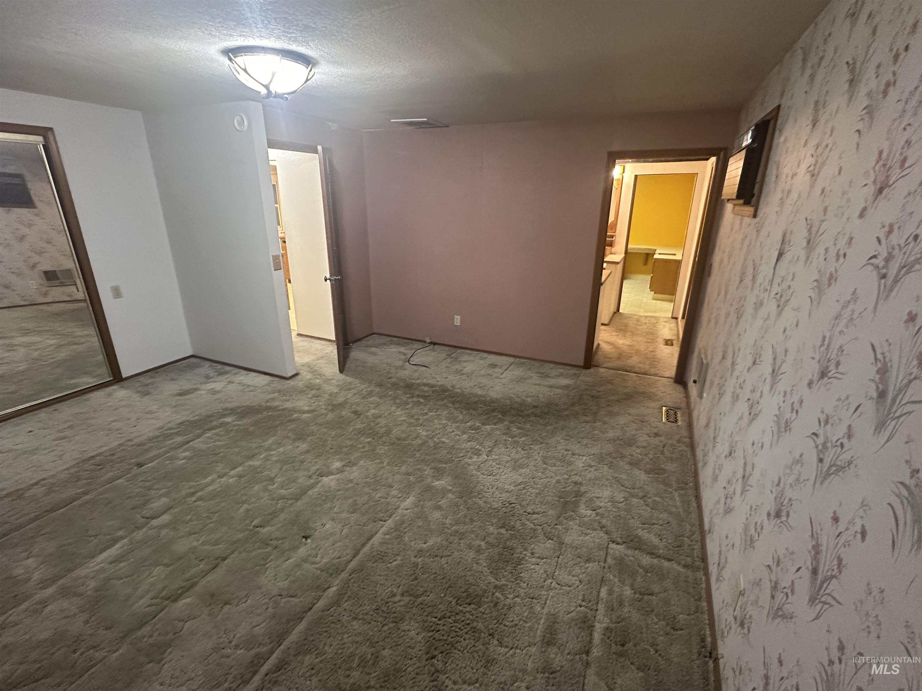 Unfurnished bedroom featuring a textured ceiling, wallpapered walls, and carpet