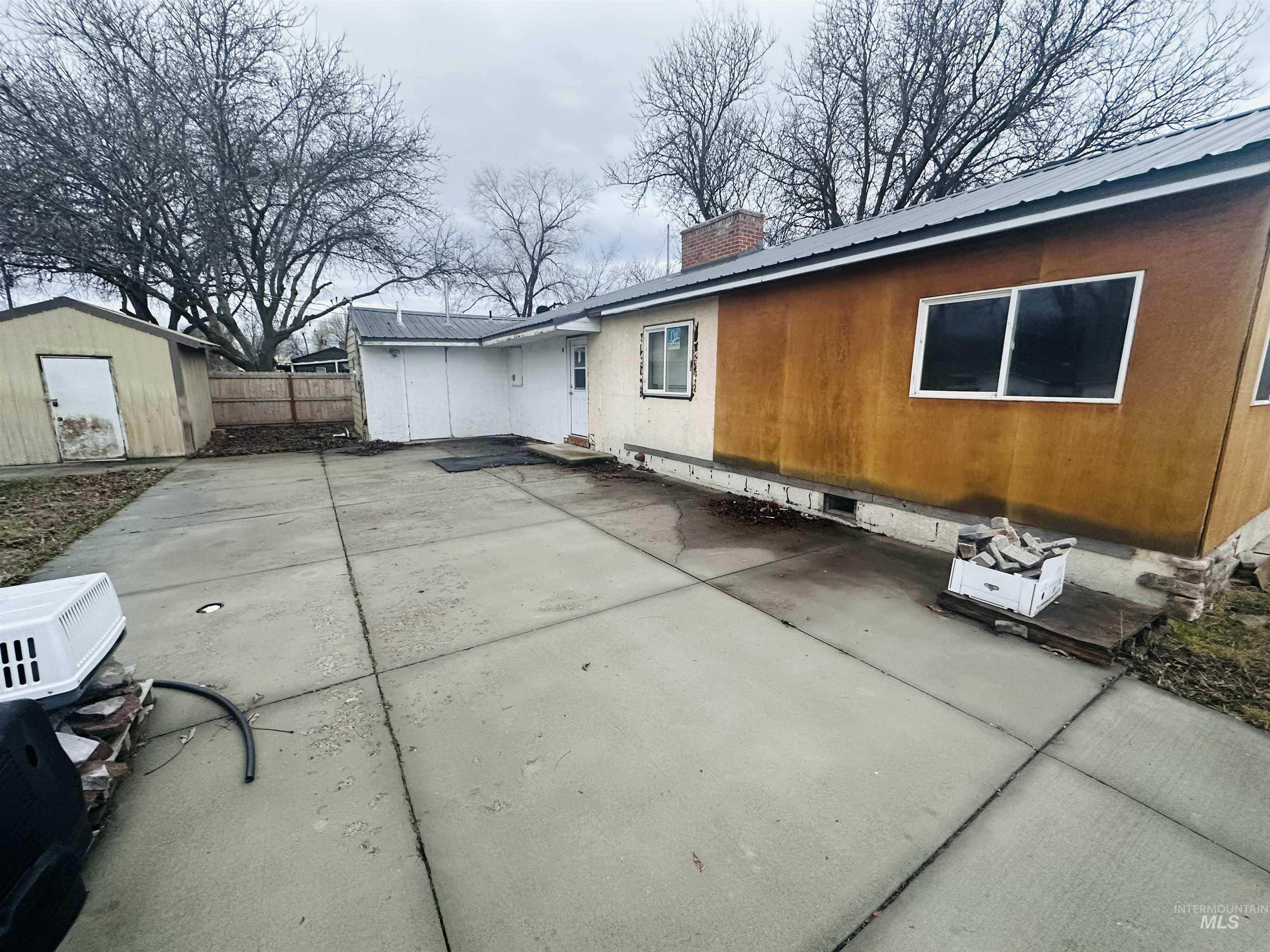 View of side of property featuring a patio, a storage unit, a metal roof, and a chimney