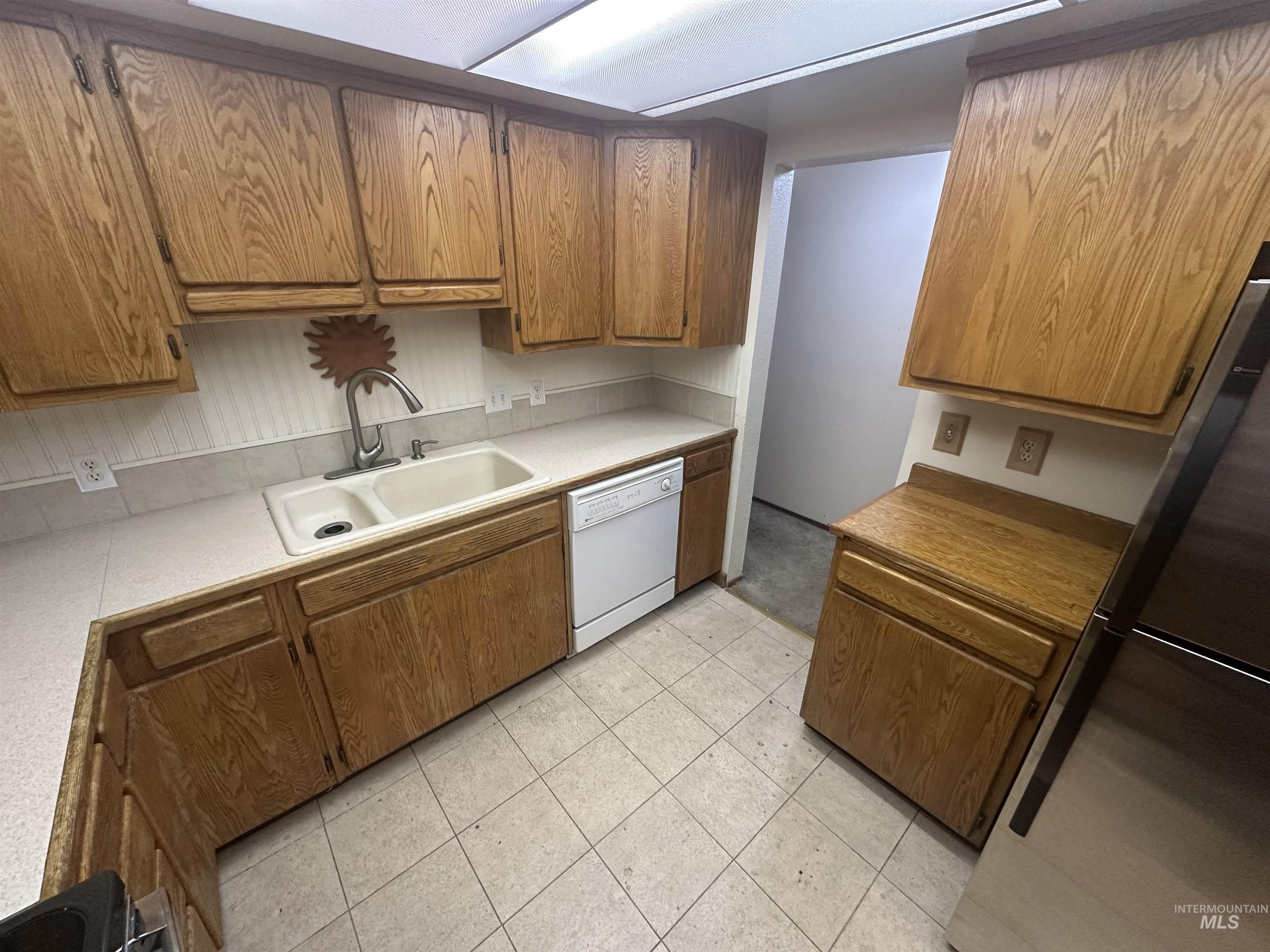 Kitchen featuring freestanding refrigerator, white dishwasher, light countertops, and brown cabinets