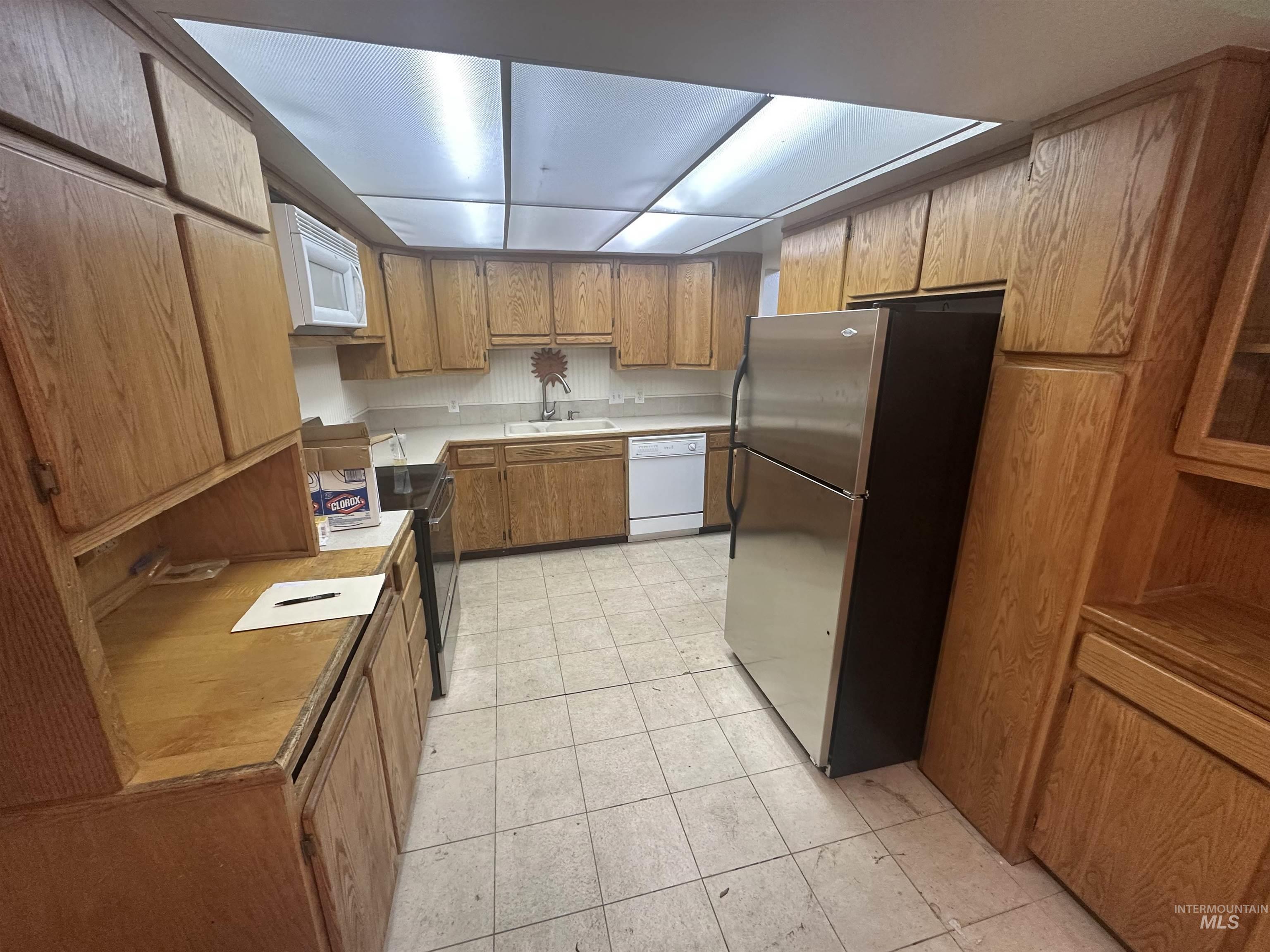 Kitchen featuring brown cabinetry, white appliances, light countertops, and light tile patterned floors