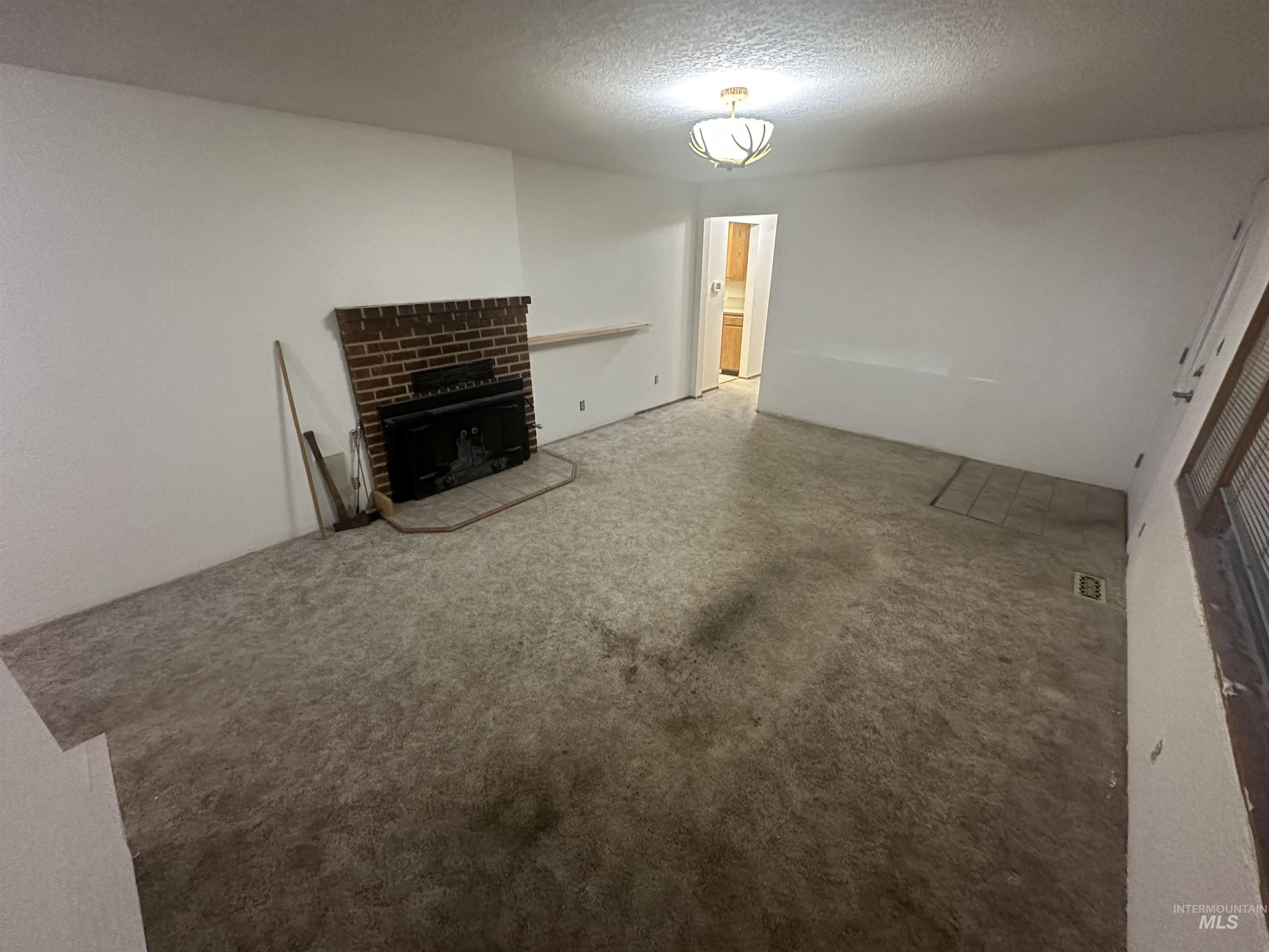 Unfurnished living room featuring a fireplace, a textured ceiling, and carpet floors
