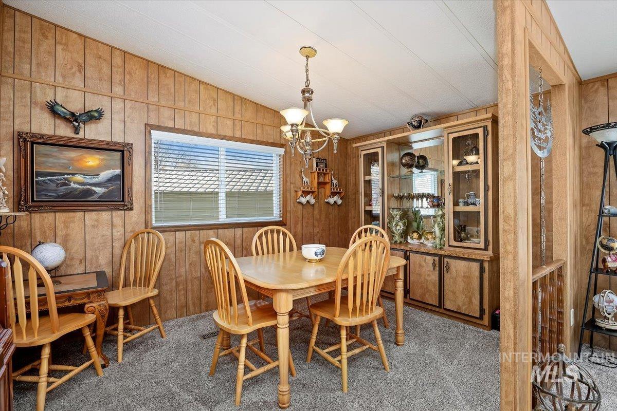 Dining area featuring vaulted ceiling, wood walls, a chandelier, and carpet floors