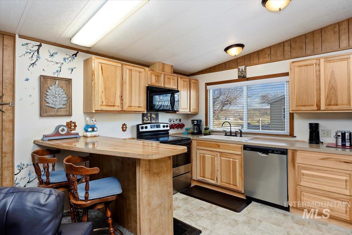 Kitchen featuring appliances with stainless steel finishes, light brown cabinets, light countertops, vaulted ceiling, and a breakfast bar