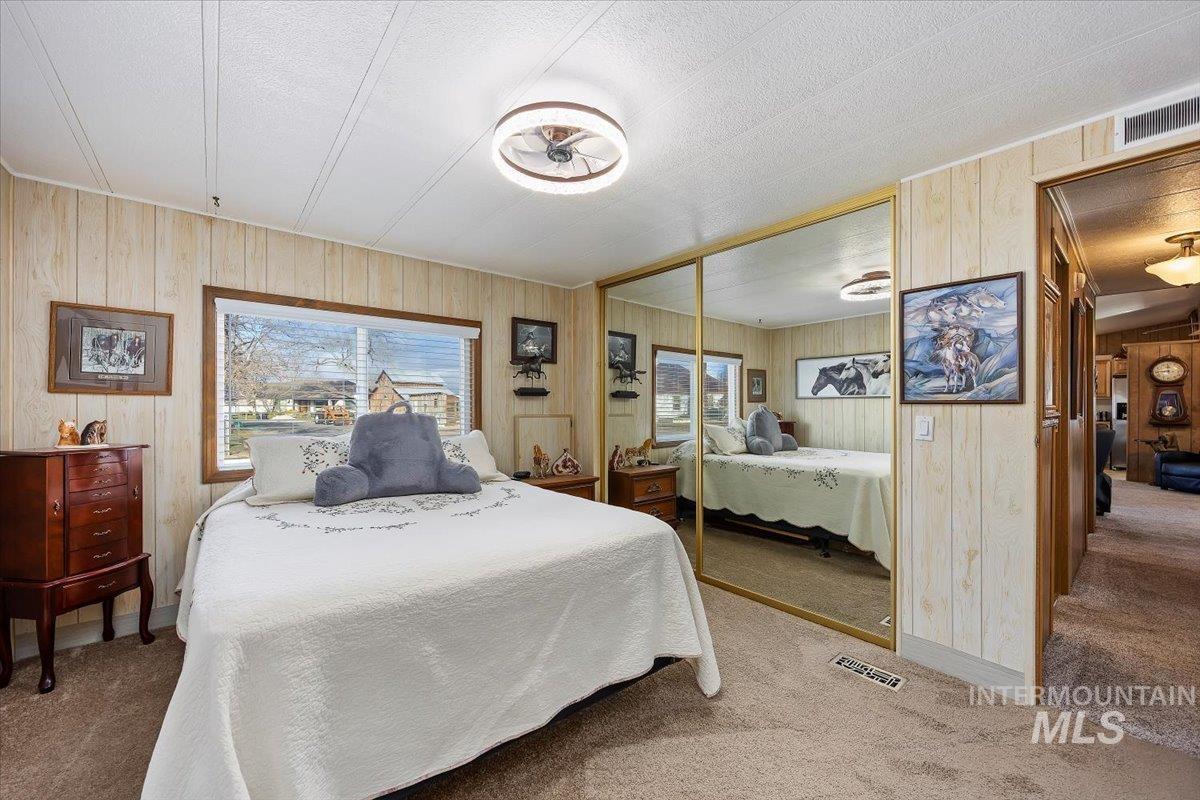Carpeted bedroom with wooden walls, a textured ceiling, and a closet