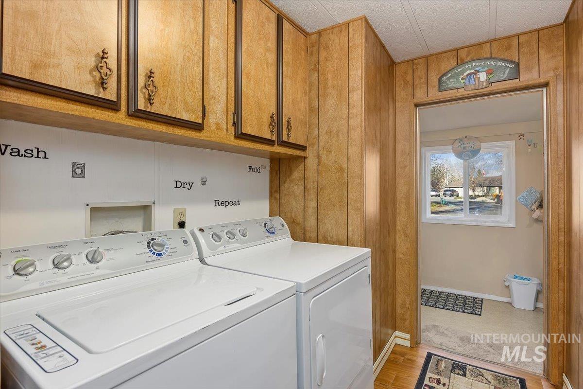 Washroom with wooden walls, light wood-type flooring, washer and dryer, and cabinet space