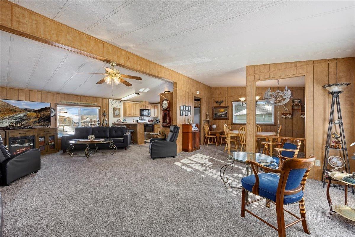 Living room with light carpet, wood walls, beamed ceiling, a textured ceiling, and ceiling fan