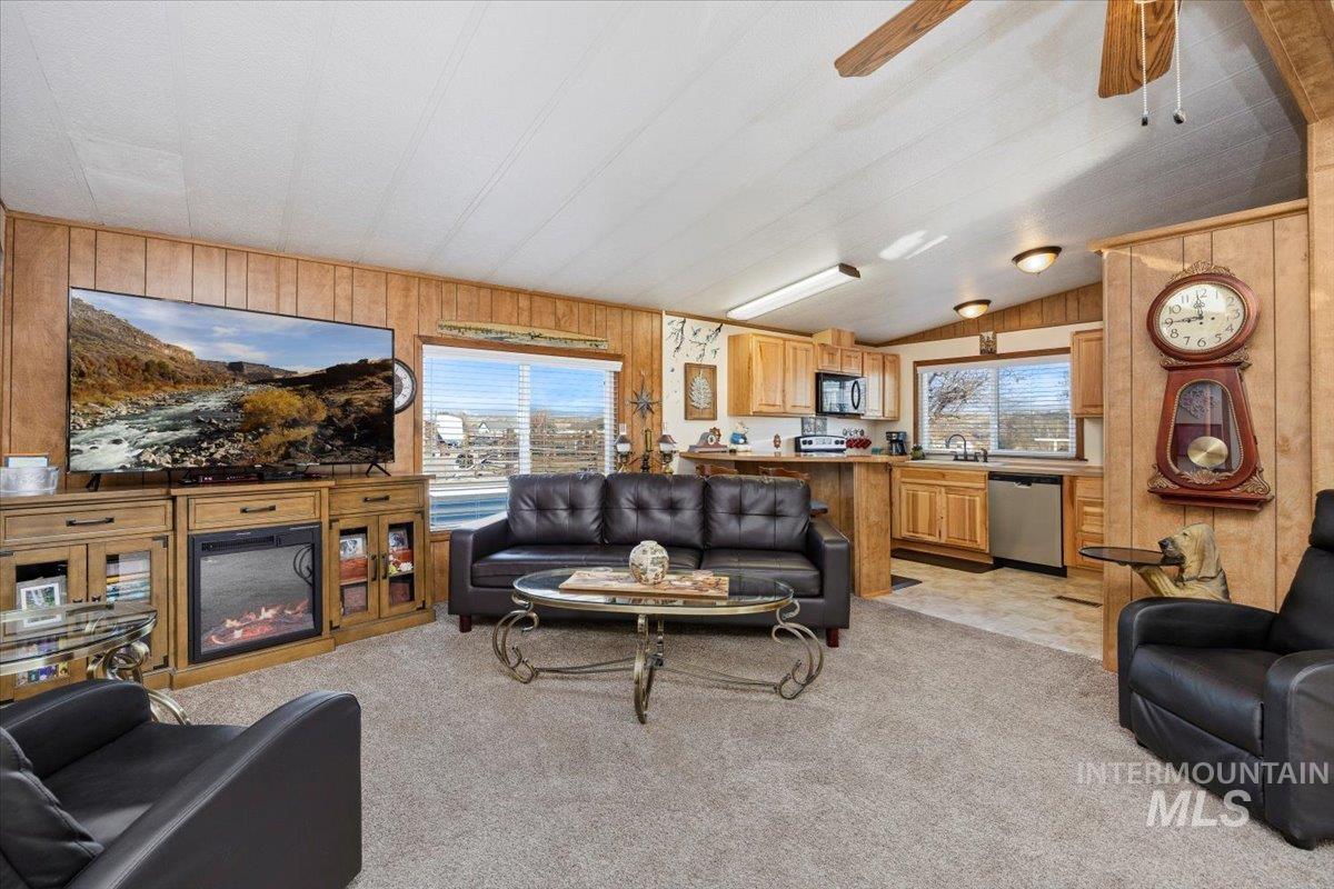 Living room with wood walls, light carpet, plenty of natural light, a ceiling fan, and vaulted ceiling