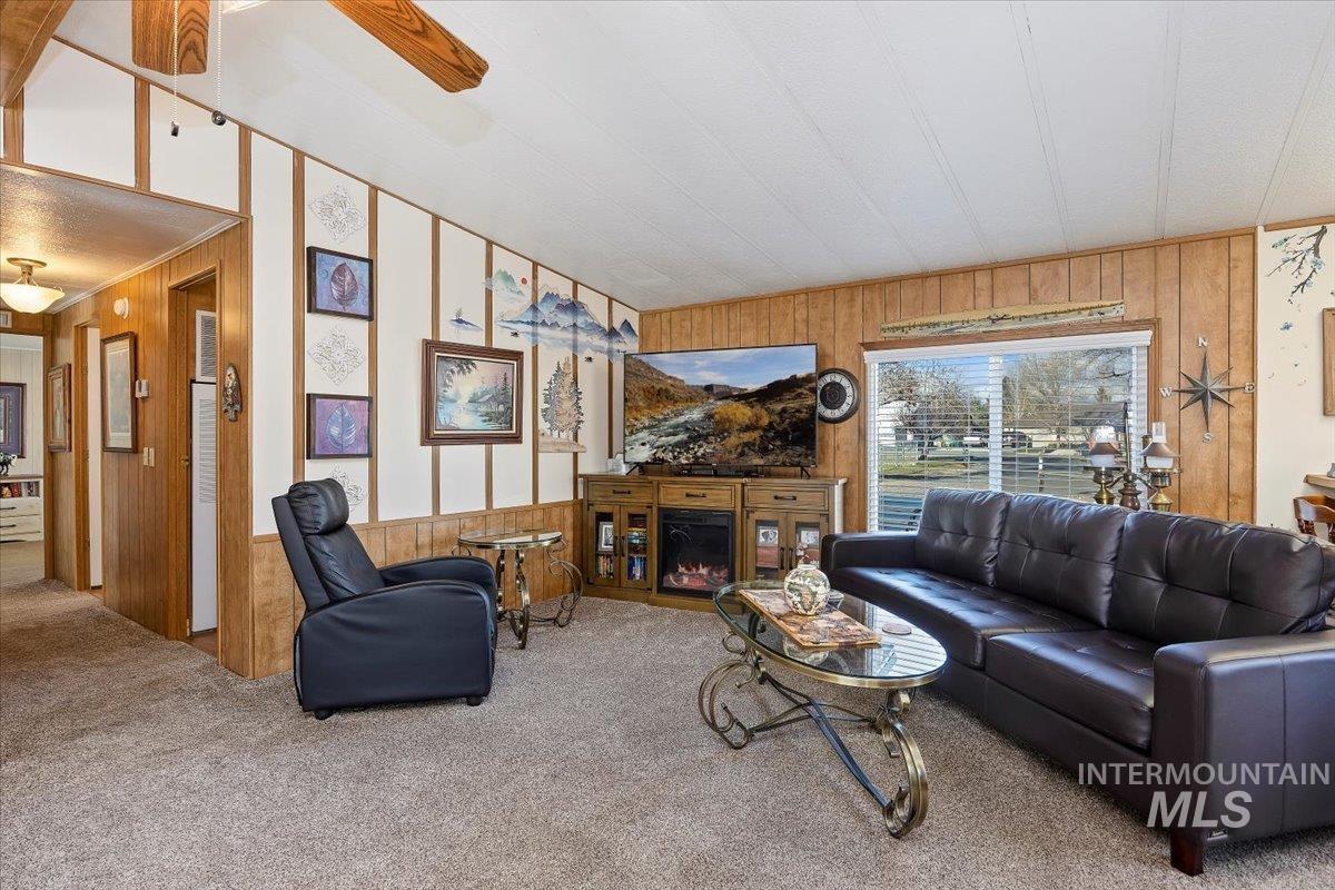 Carpeted living area featuring wood walls, a lit fireplace, and a ceiling fan