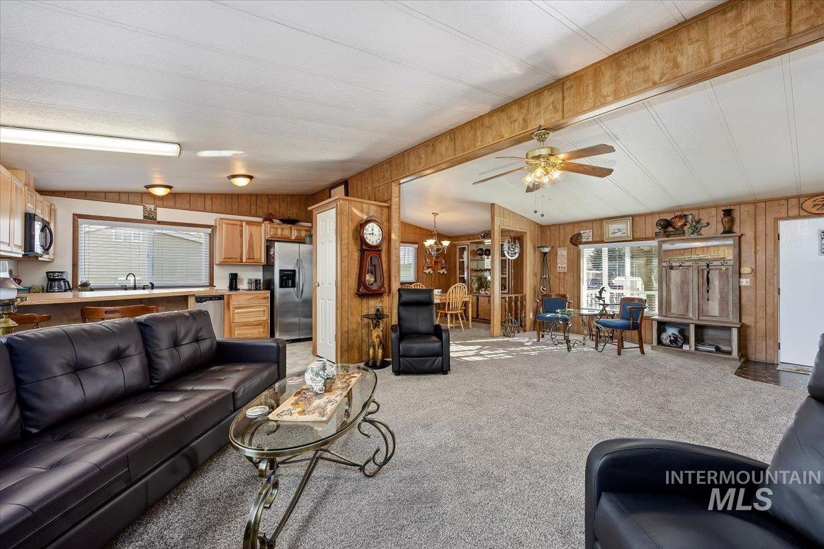 Living room with a chandelier, light carpet, wooden walls, vaulted ceiling, and ceiling fan