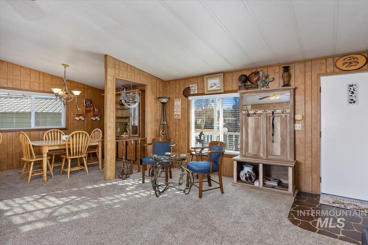 Carpeted dining space with lofted ceiling, wooden walls, a chandelier, and plenty of natural light