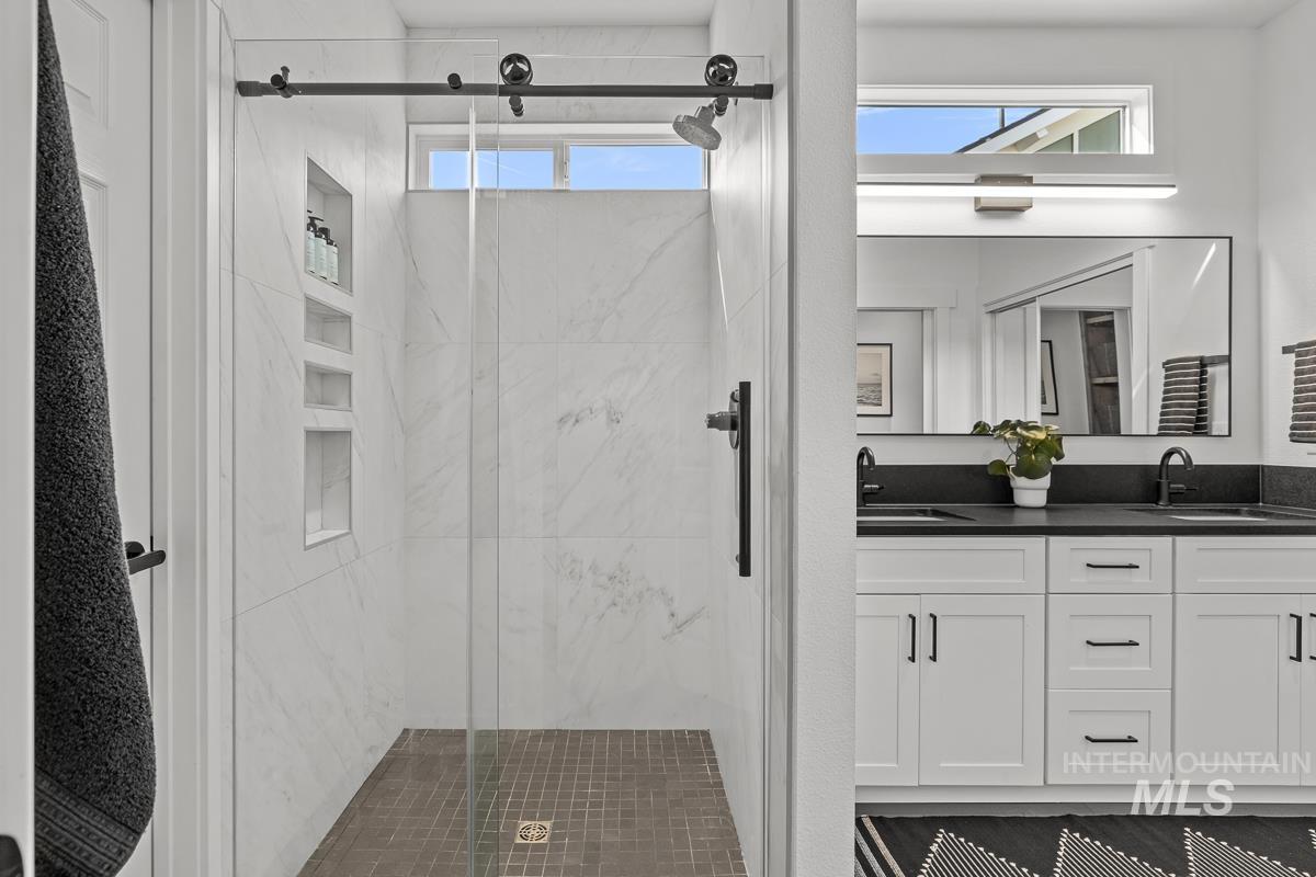 Full bathroom featuring double vanity and a marble finish shower