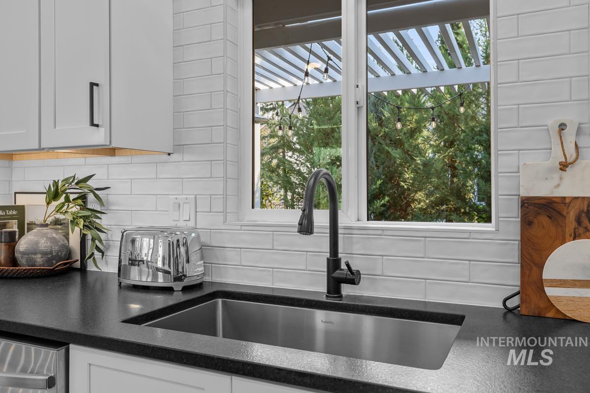 Kitchen view of backsplash, dark stone countertops, and white cabinetry