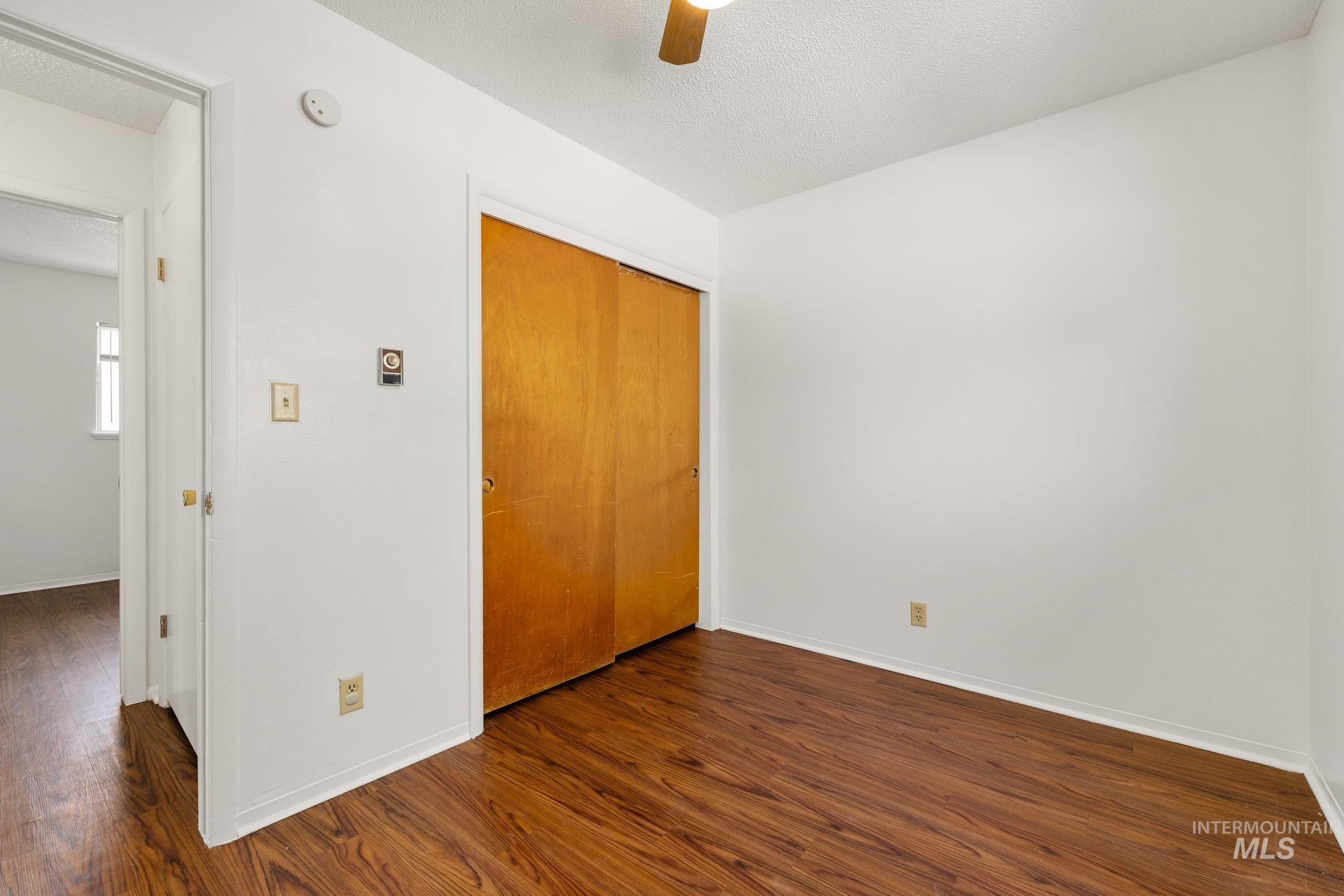 Unfurnished bedroom featuring dark wood finished floors, a closet, ceiling fan, and a textured ceiling