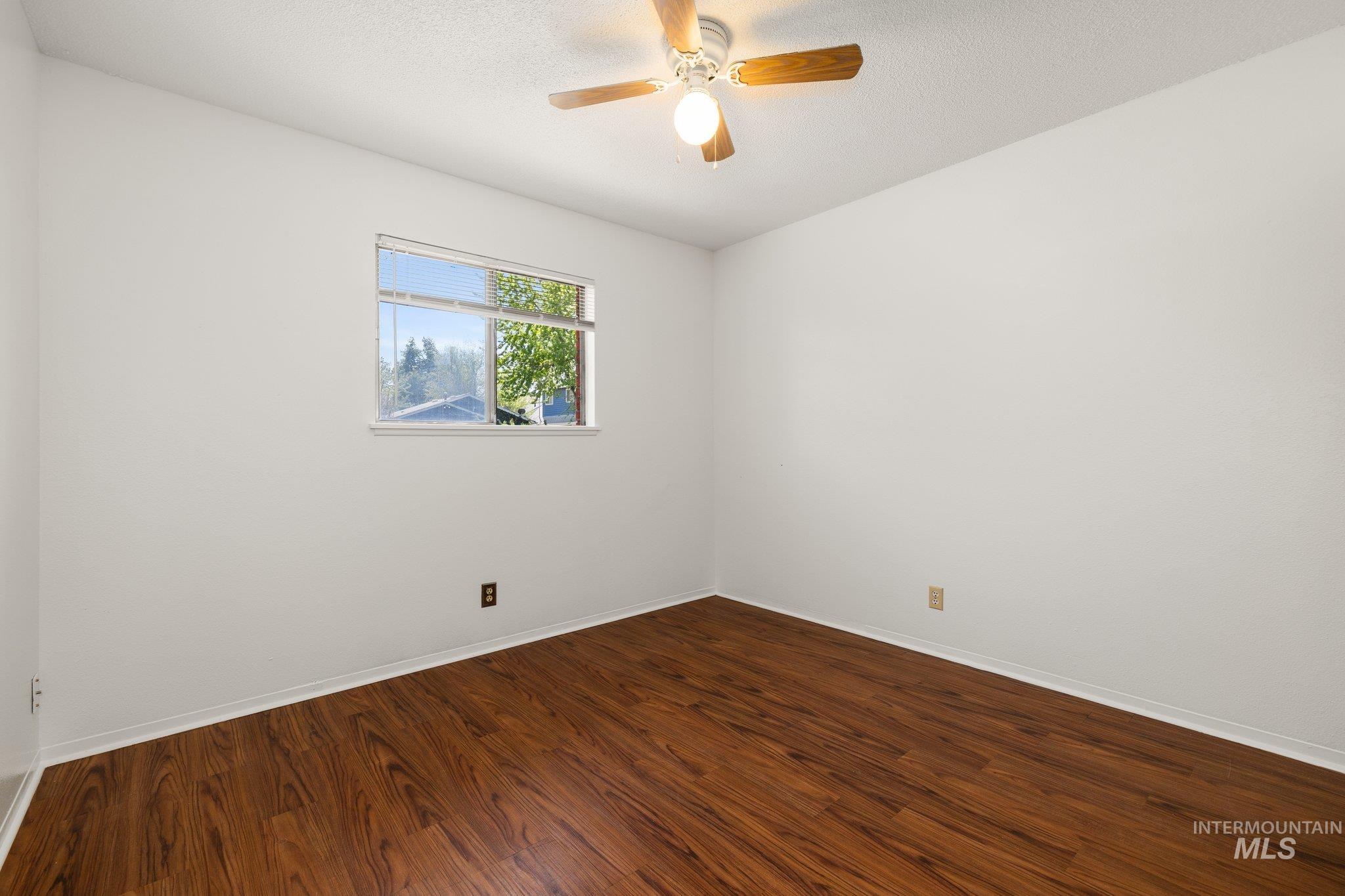 Empty room featuring dark wood-style flooring, a textured ceiling, and ceiling fan