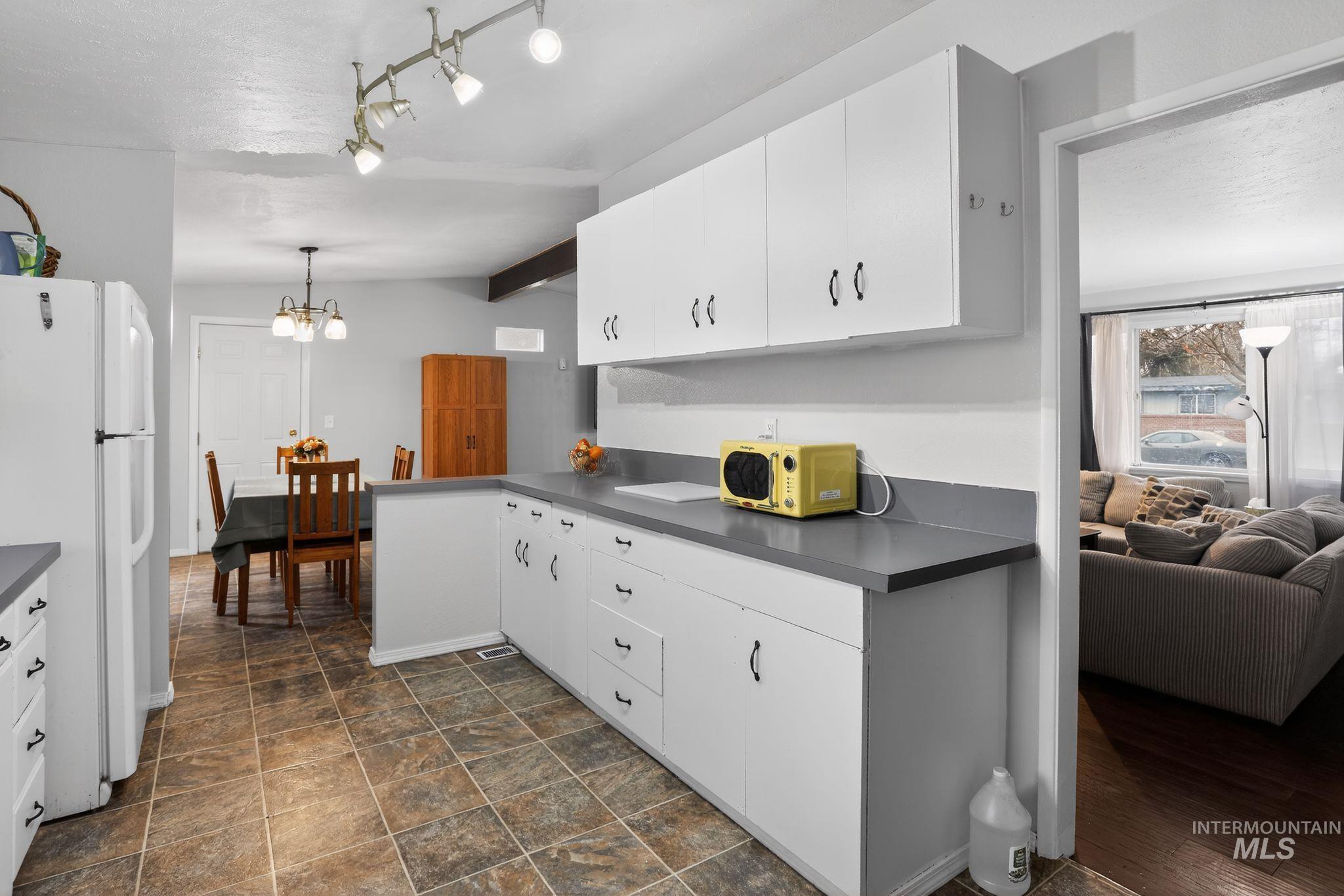 Kitchen featuring white cabinets, freestanding refrigerator, dark countertops, lofted ceiling, and stone finish flooring
