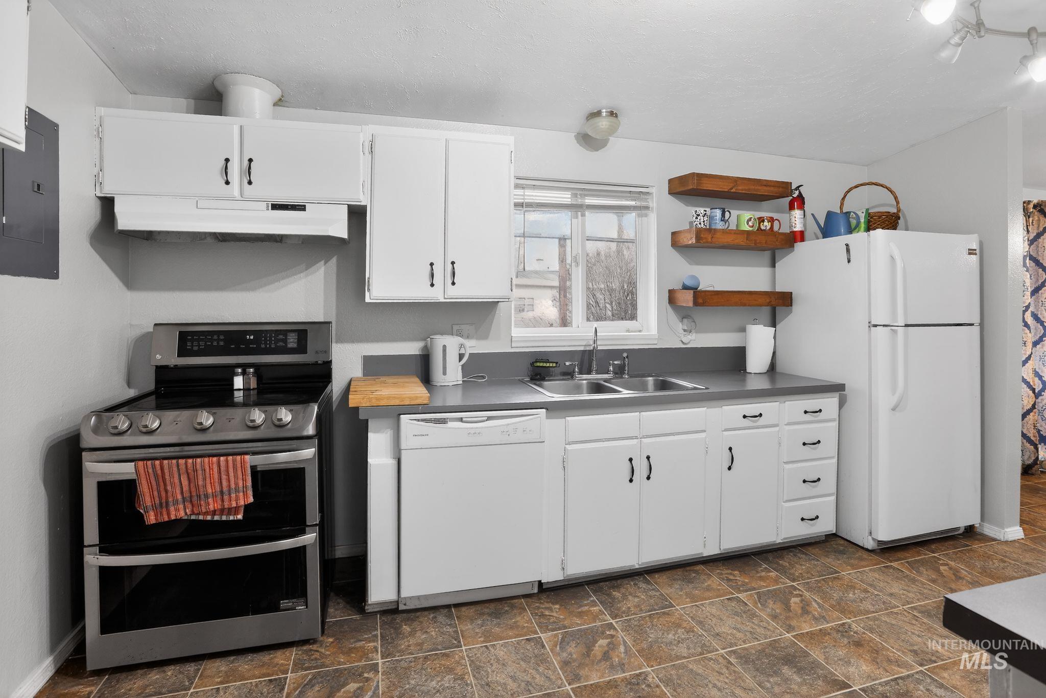 Kitchen with white appliances, open shelves, white cabinetry, electric panel, and stone finish floors