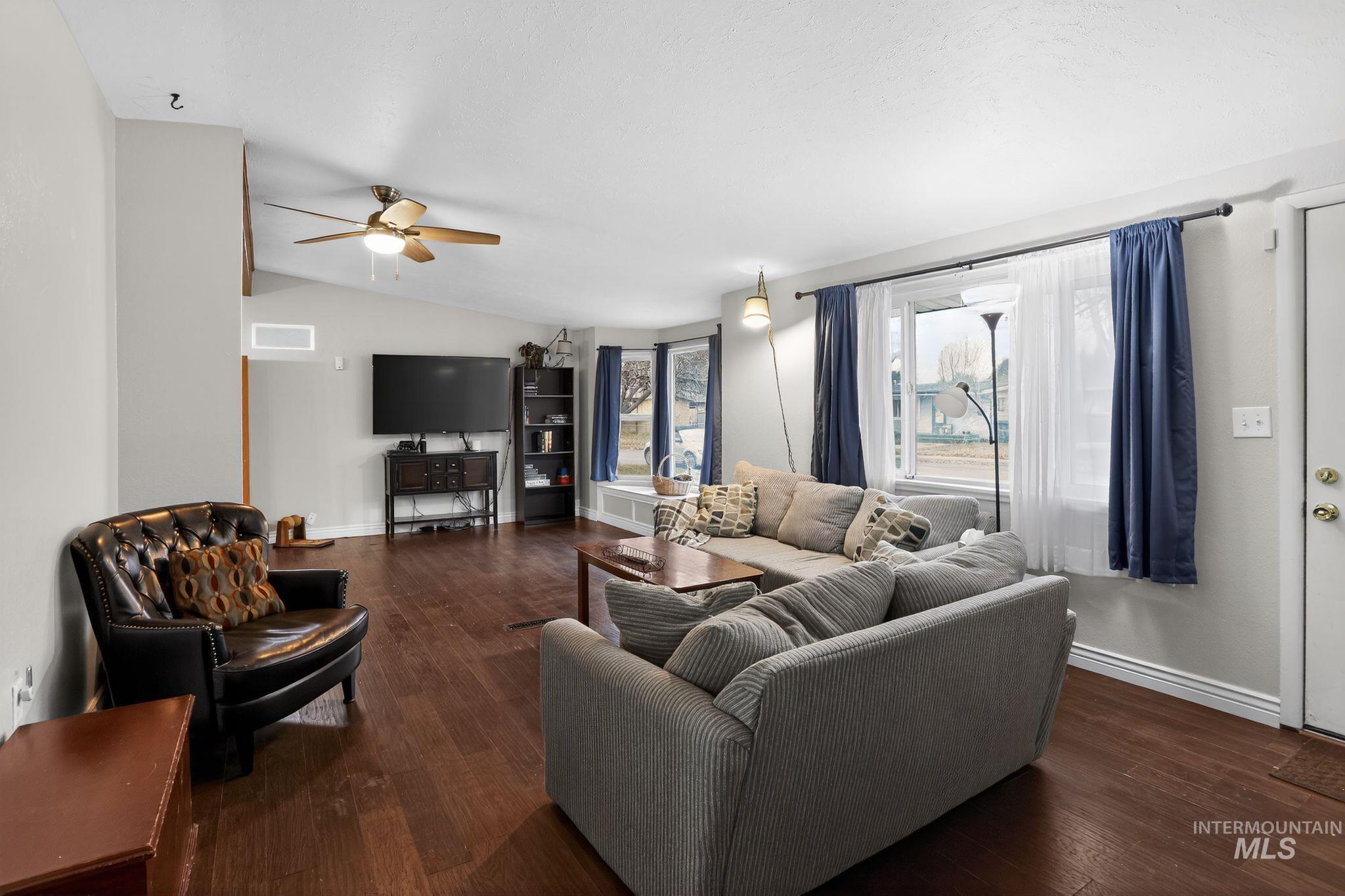 Living area featuring lofted ceiling, dark wood-style floors, and ceiling fan