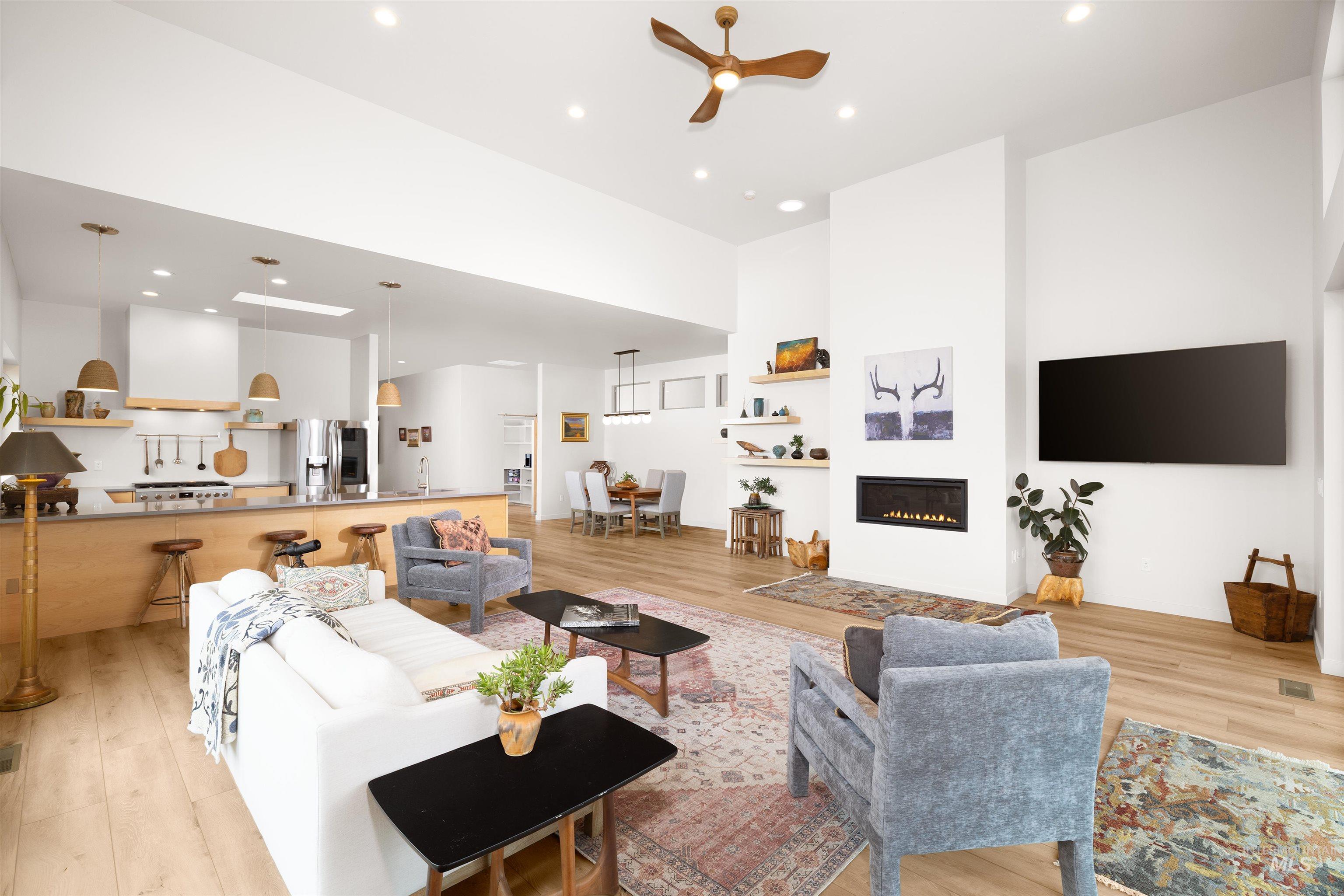 Living room with light wood-type flooring, a ceiling fan, recessed lighting, a glass covered fireplace, and a high ceiling