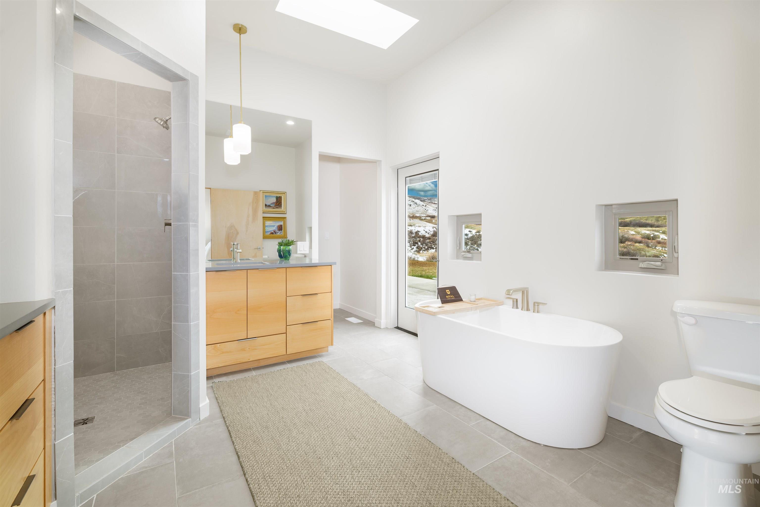 Full bath featuring vanity, a walk in shower, a skylight, a freestanding tub, and light tile patterned flooring