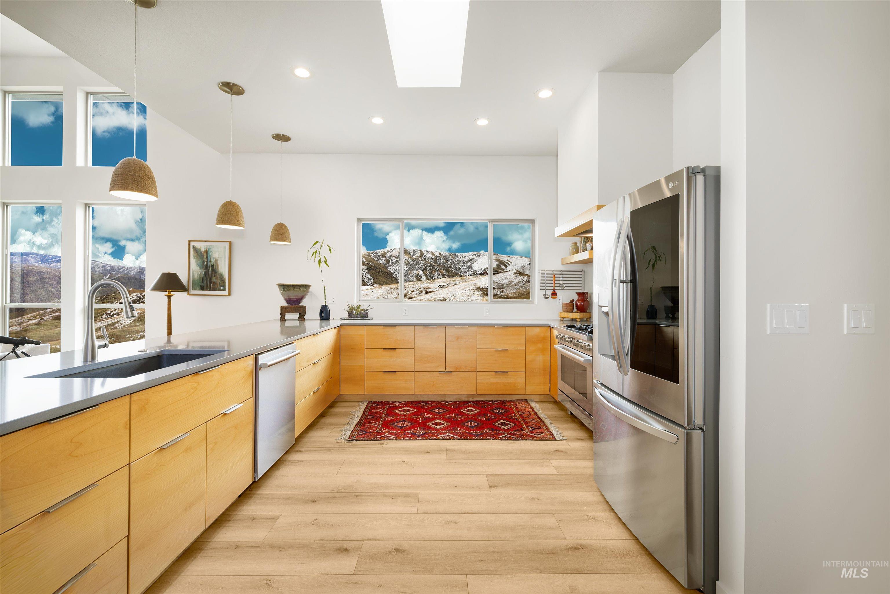 Kitchen featuring a skylight, pendant lighting, stainless steel appliances, modern cabinets, and light brown cabinetry