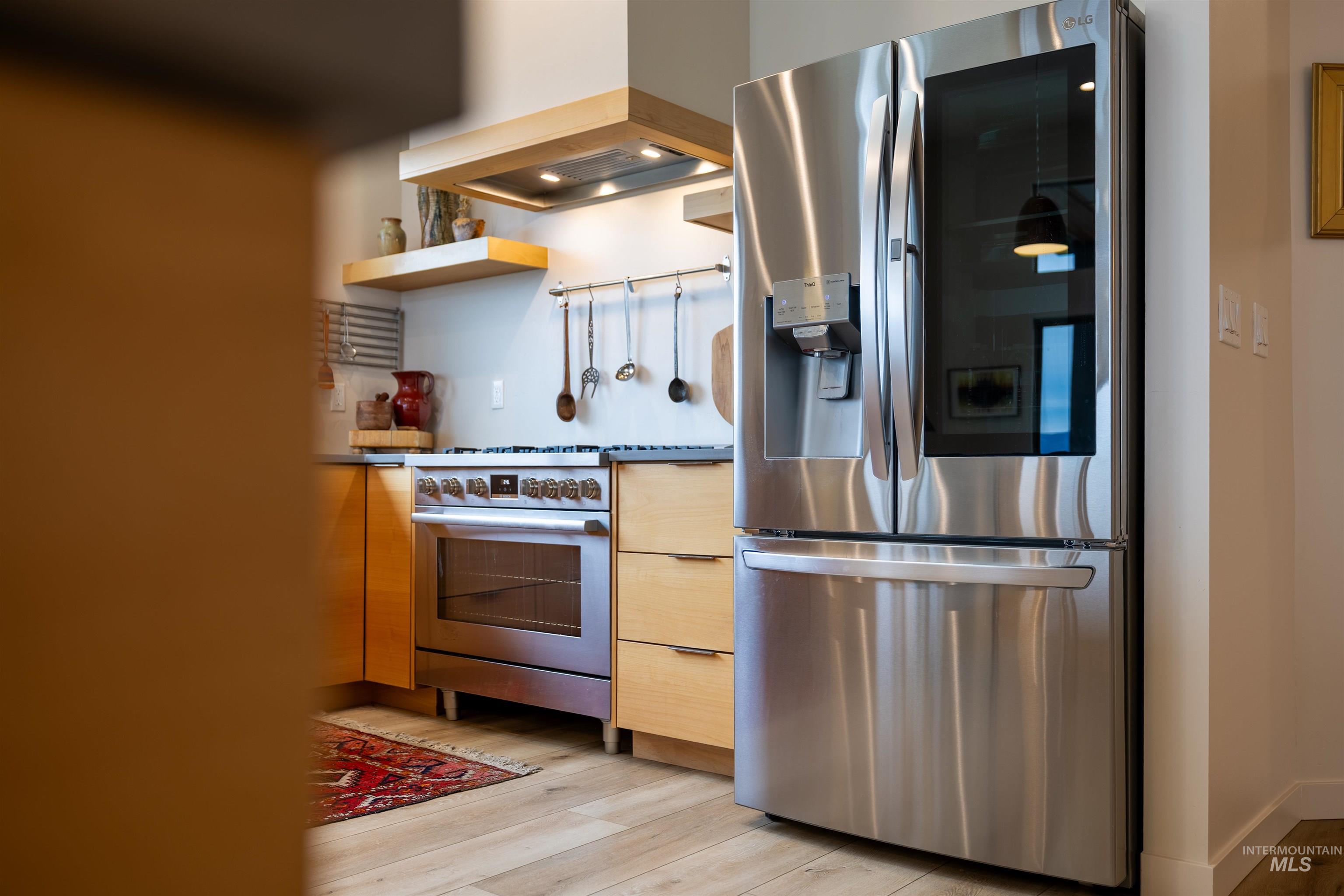 Kitchen with appliances with stainless steel finishes, custom exhaust hood, open shelves, light wood-type flooring, and modern cabinets