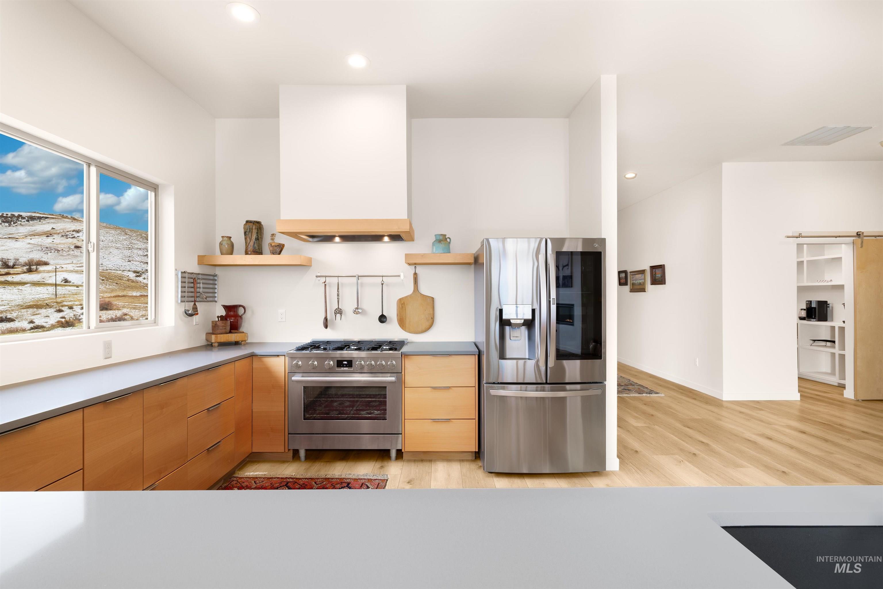 Kitchen featuring appliances with stainless steel finishes, modern cabinets, premium range hood, open shelves, and light wood-style floors