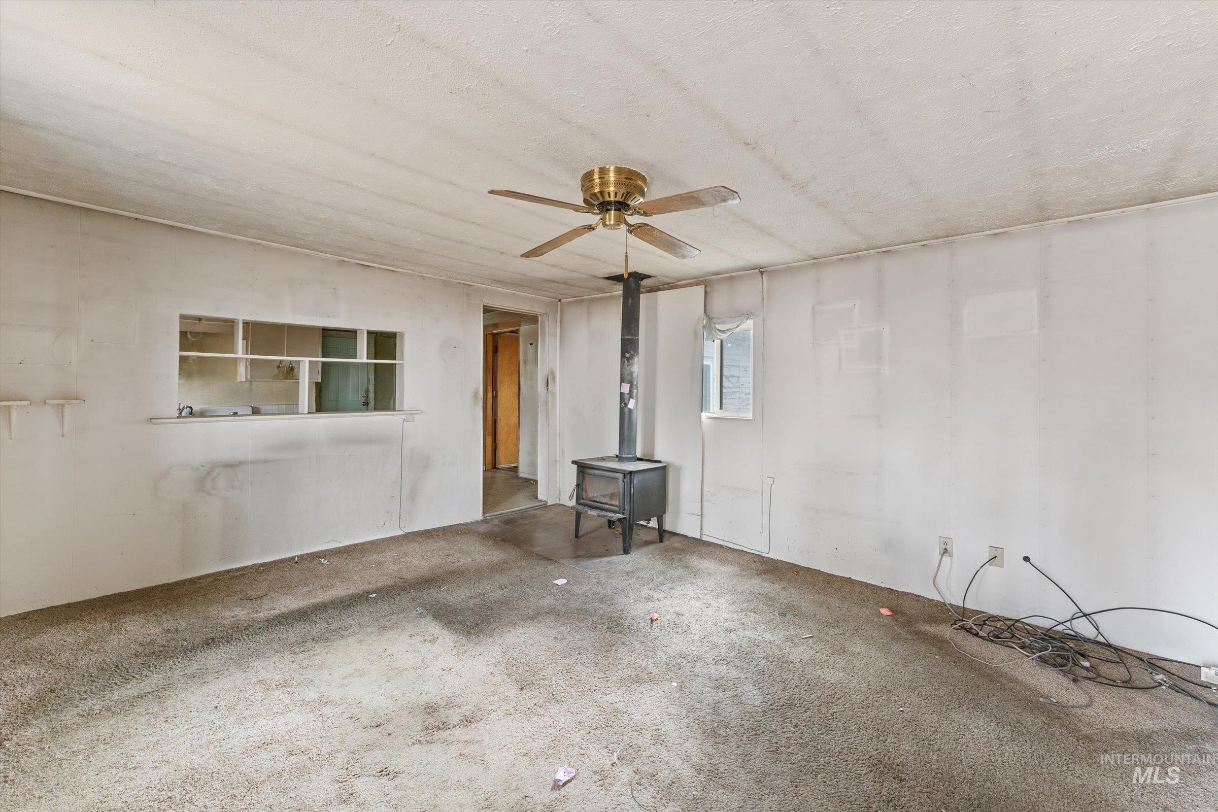 Carpeted spare room with a wood stove and ceiling fan