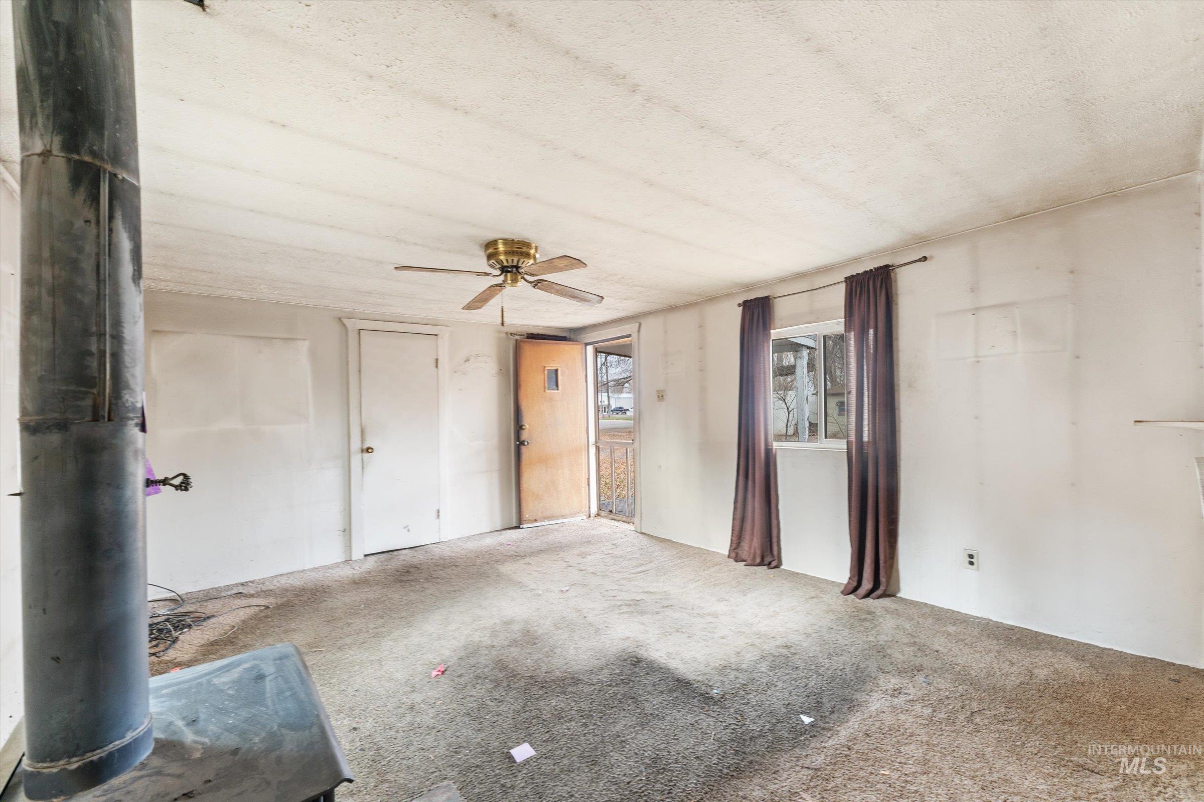 Carpeted empty room with a ceiling fan, a wood stove, and a textured ceiling
