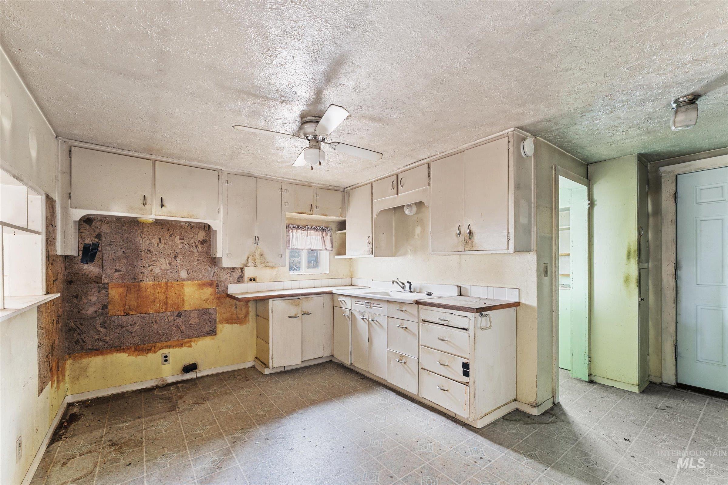 Kitchen with light floors, cream cabinets, light countertops, a ceiling fan, and a textured ceiling
