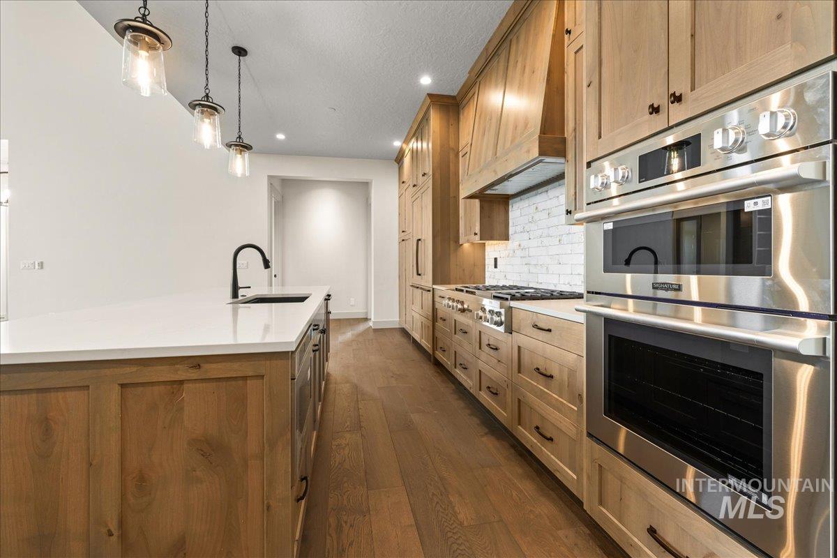 Kitchen featuring appliances with stainless steel finishes, brown cabinets, decorative backsplash, decorative light fixtures, and a kitchen island with sink