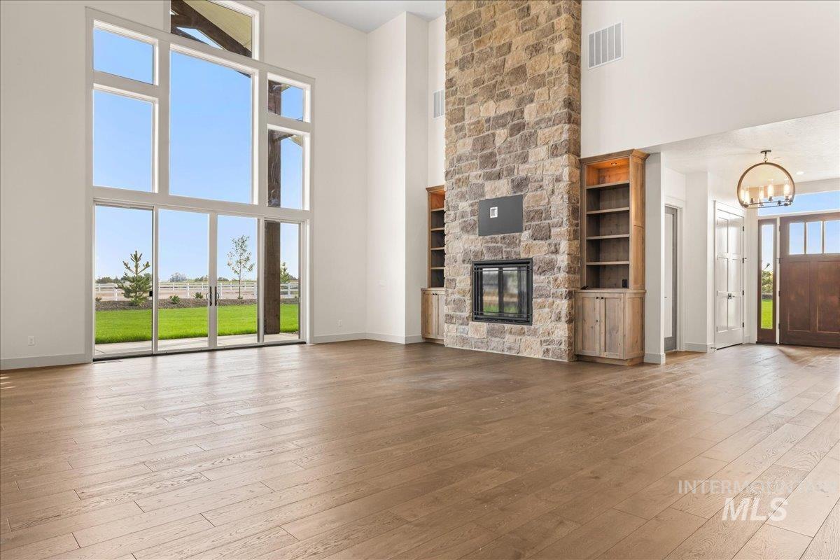 Unfurnished living room featuring light wood finished floors, a towering ceiling, a fireplace, and a chandelier