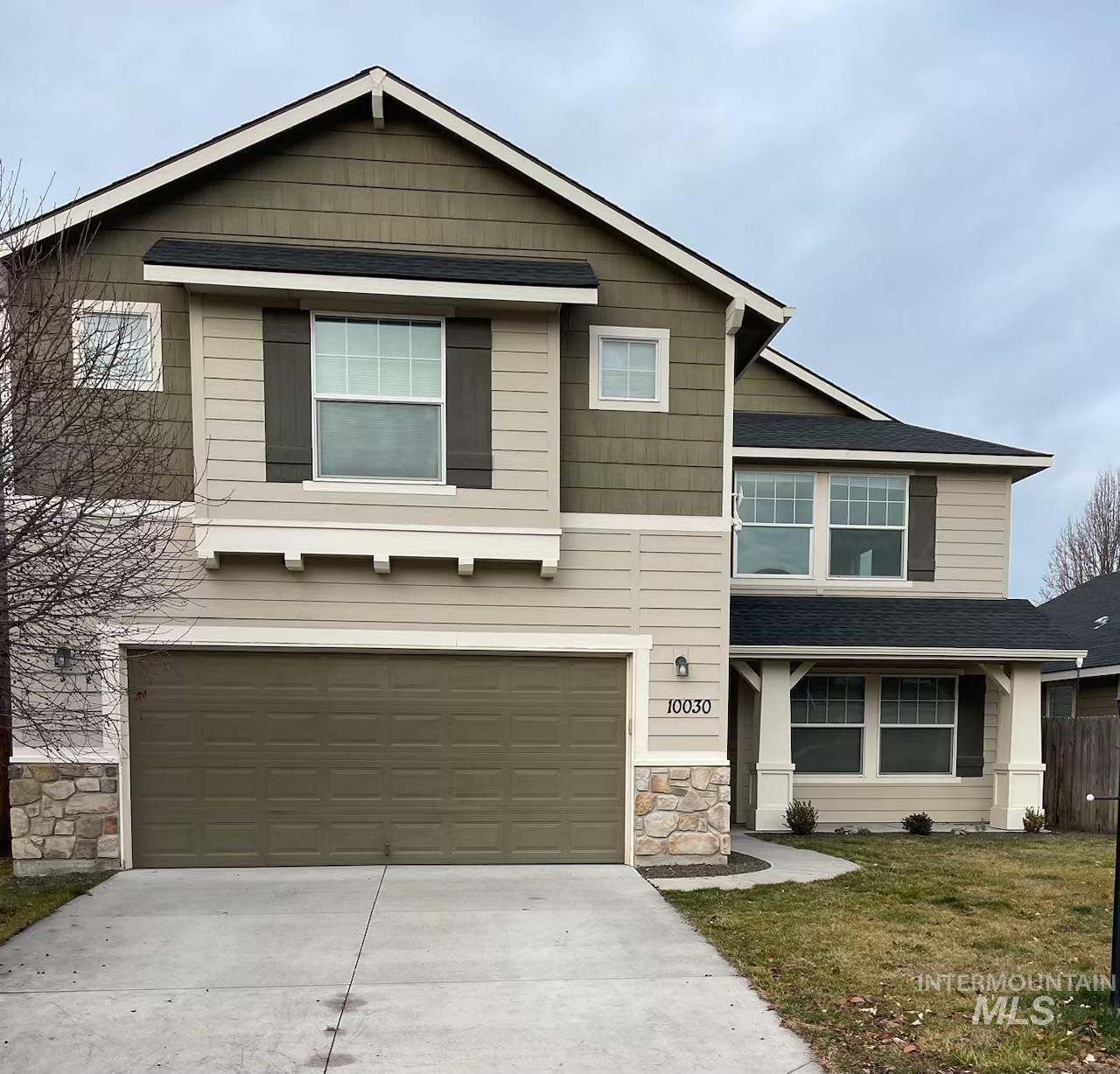 Craftsman-style home with stone siding, a shingled roof, concrete driveway, an attached garage, and a front yard