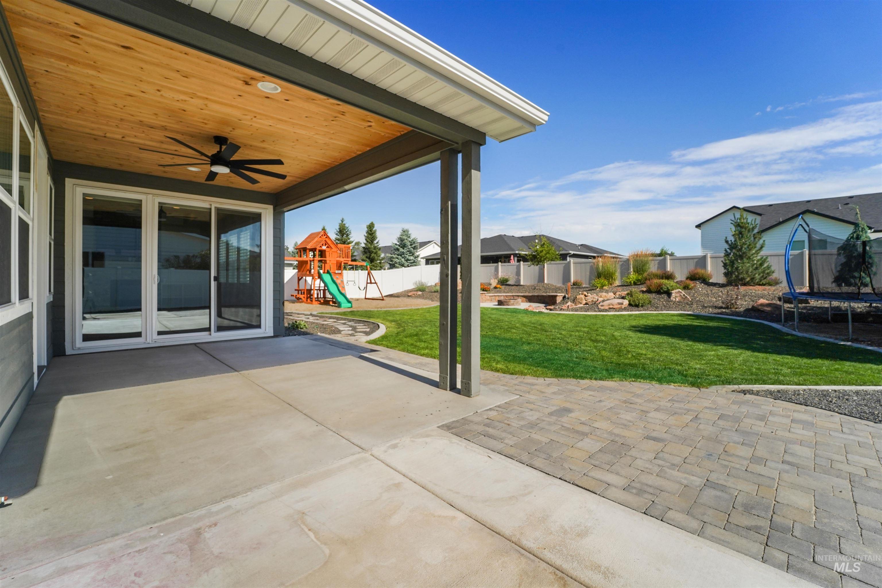 Fenced backyard featuring a trampoline, a patio area, ceiling fan, a playground, and a residential view
