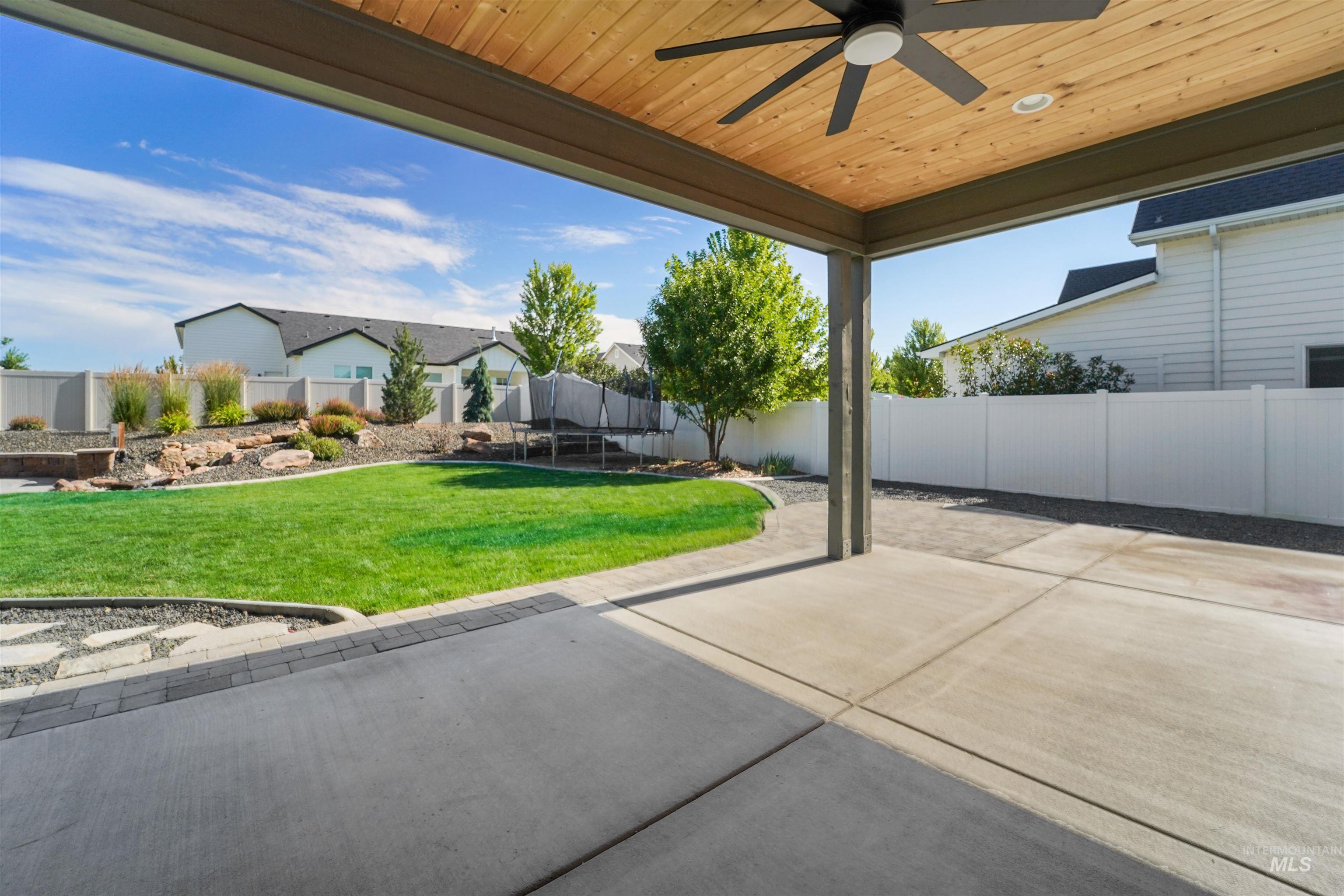 Fenced backyard with a trampoline, a patio area, and a ceiling fan