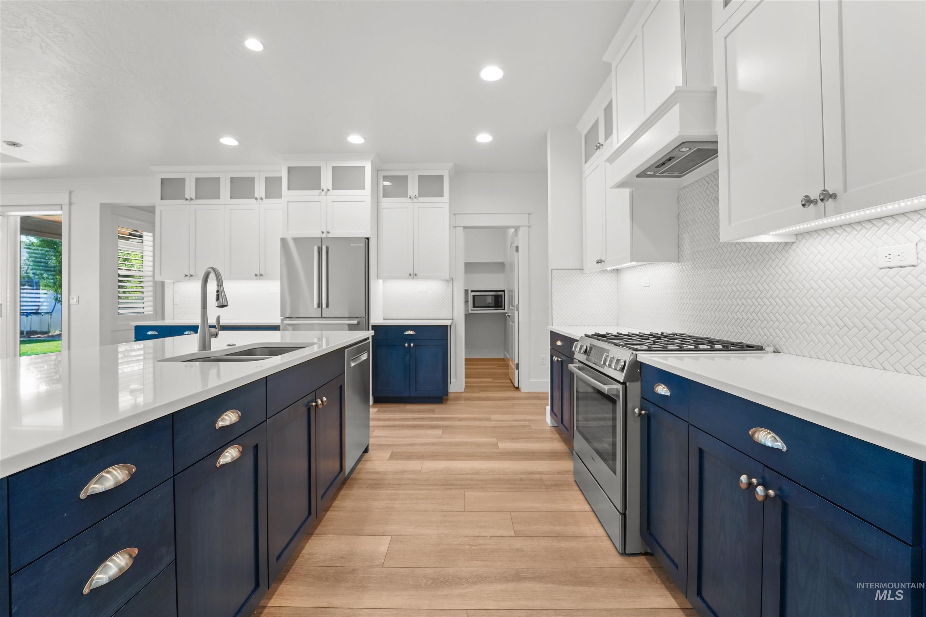 Kitchen with appliances with stainless steel finishes, blue cabinetry, light wood-type flooring, light countertops, and white cabinetry