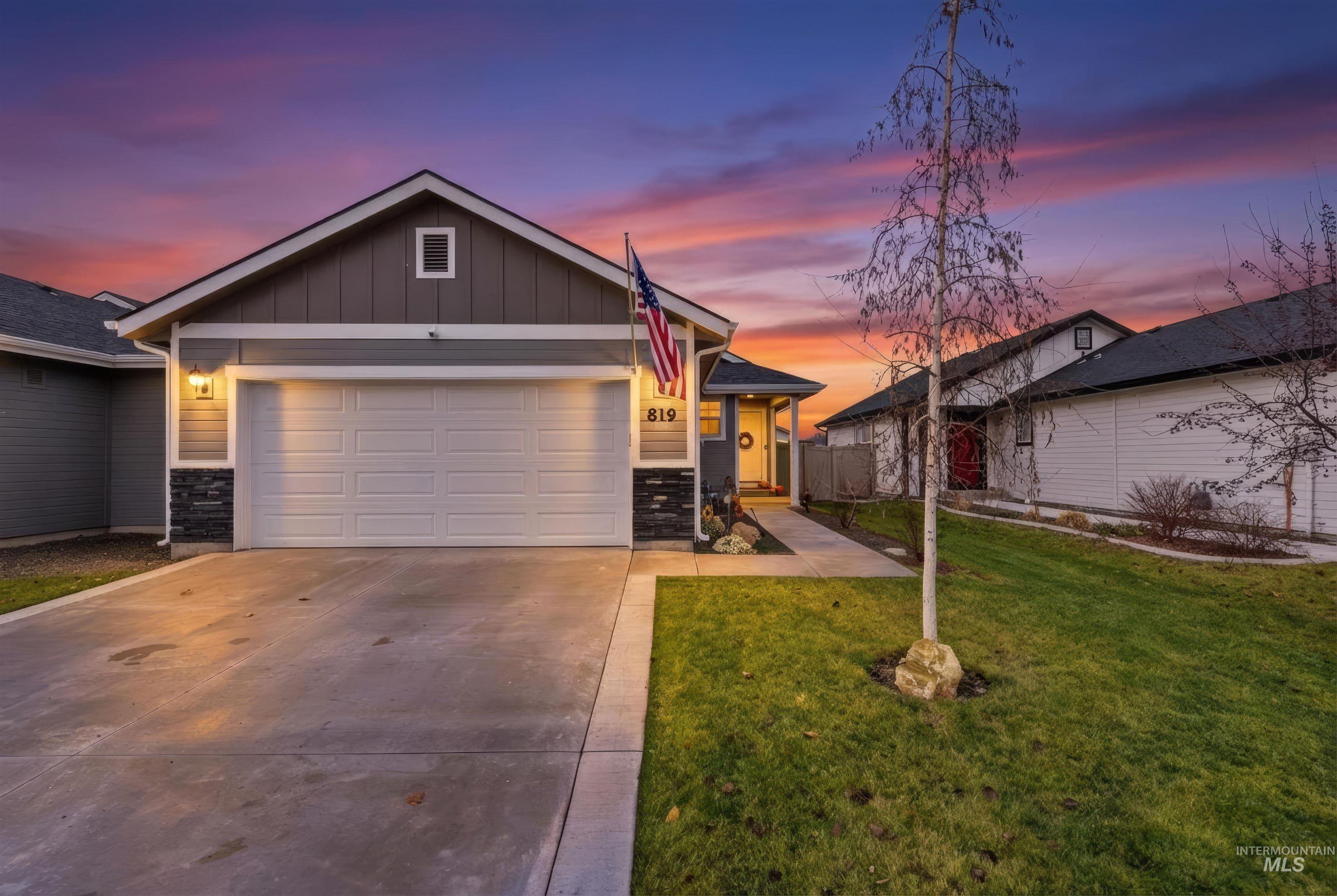 View of front facade with board and batten siding, concrete driveway, a lawn, a garage, and stone siding