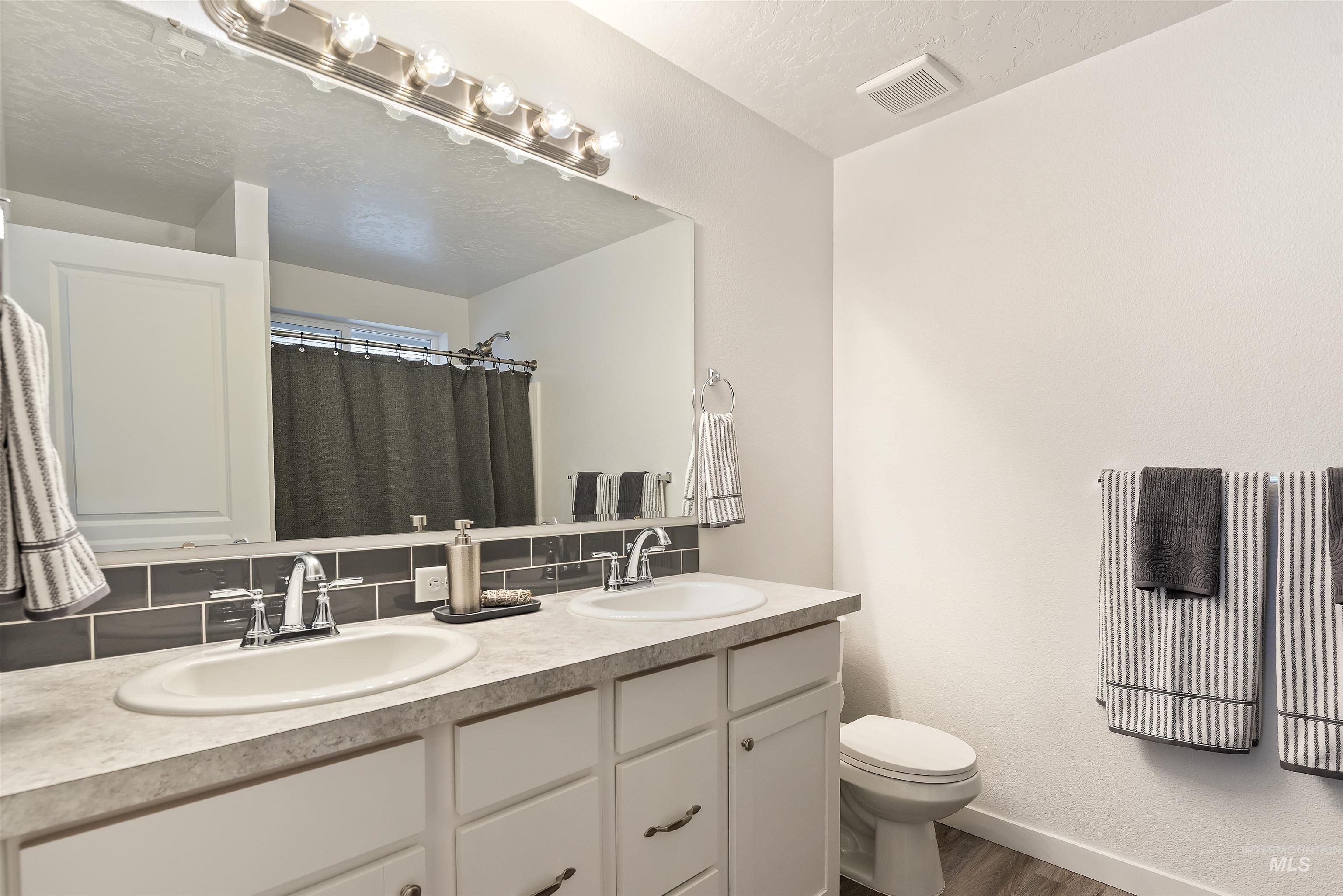 Full bathroom with curtained shower, double vanity, tasteful backsplash, and a textured ceiling