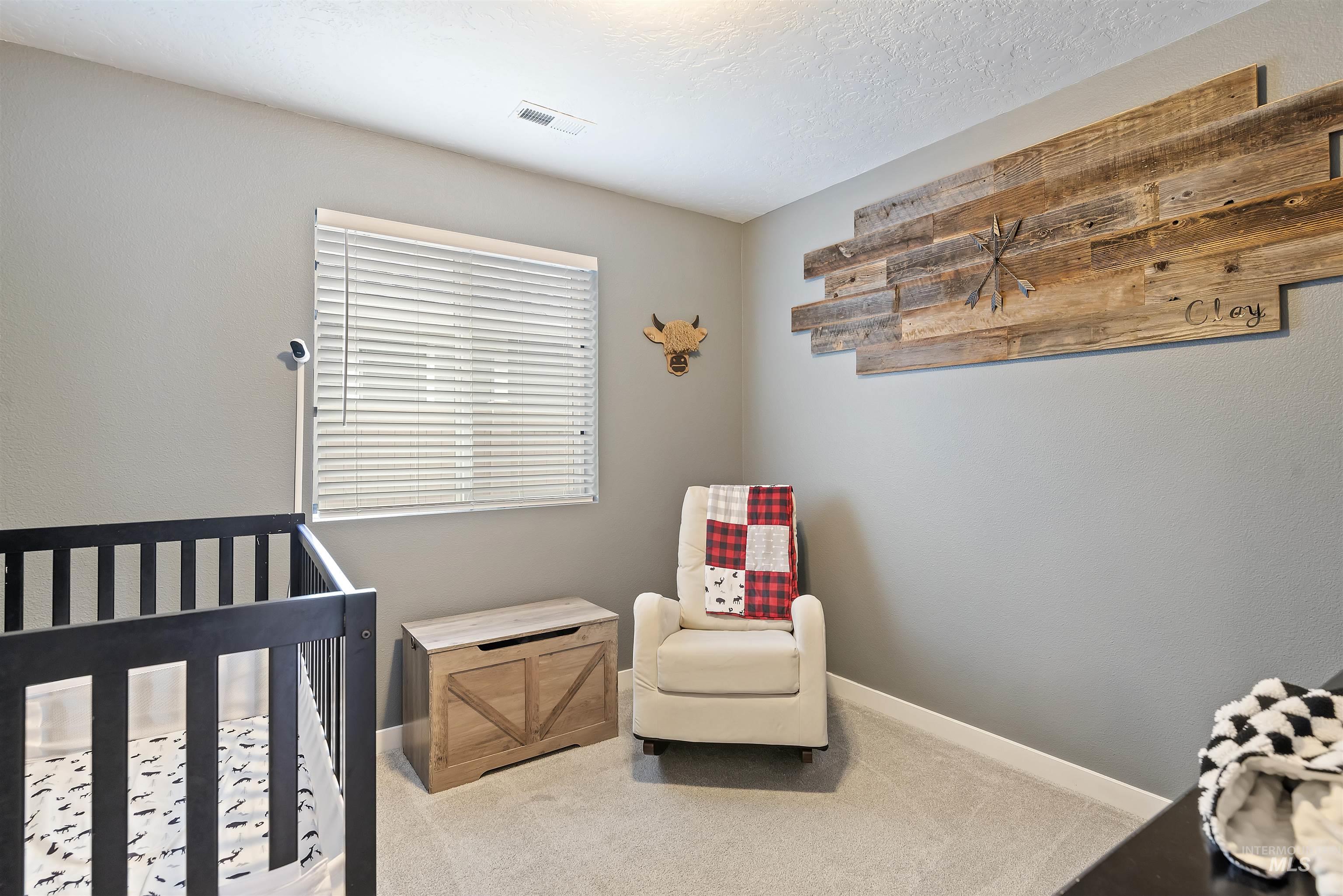 Carpeted bedroom featuring a crib and a textured ceiling