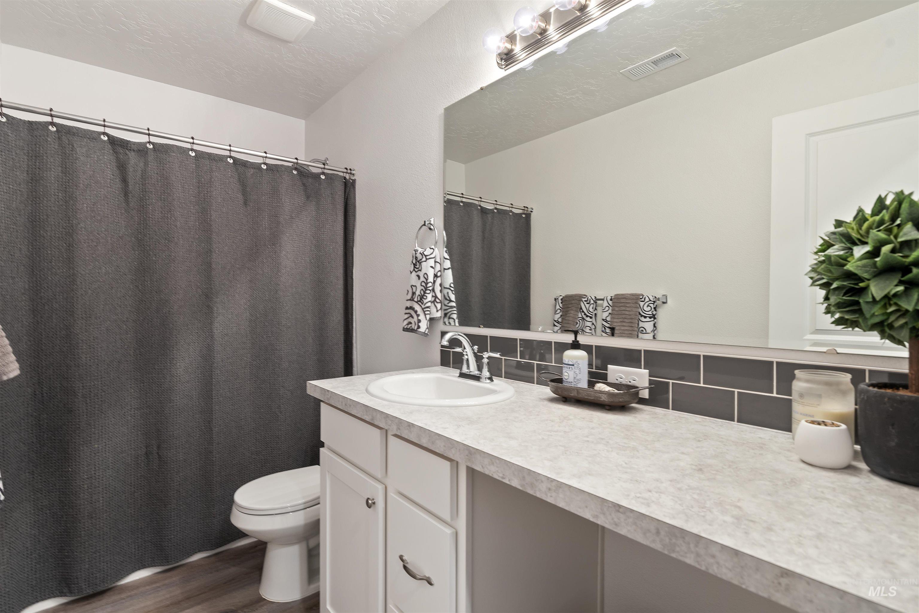 Bathroom featuring a shower with curtain, vanity, decorative backsplash, a textured ceiling, and dark wood-style floors
