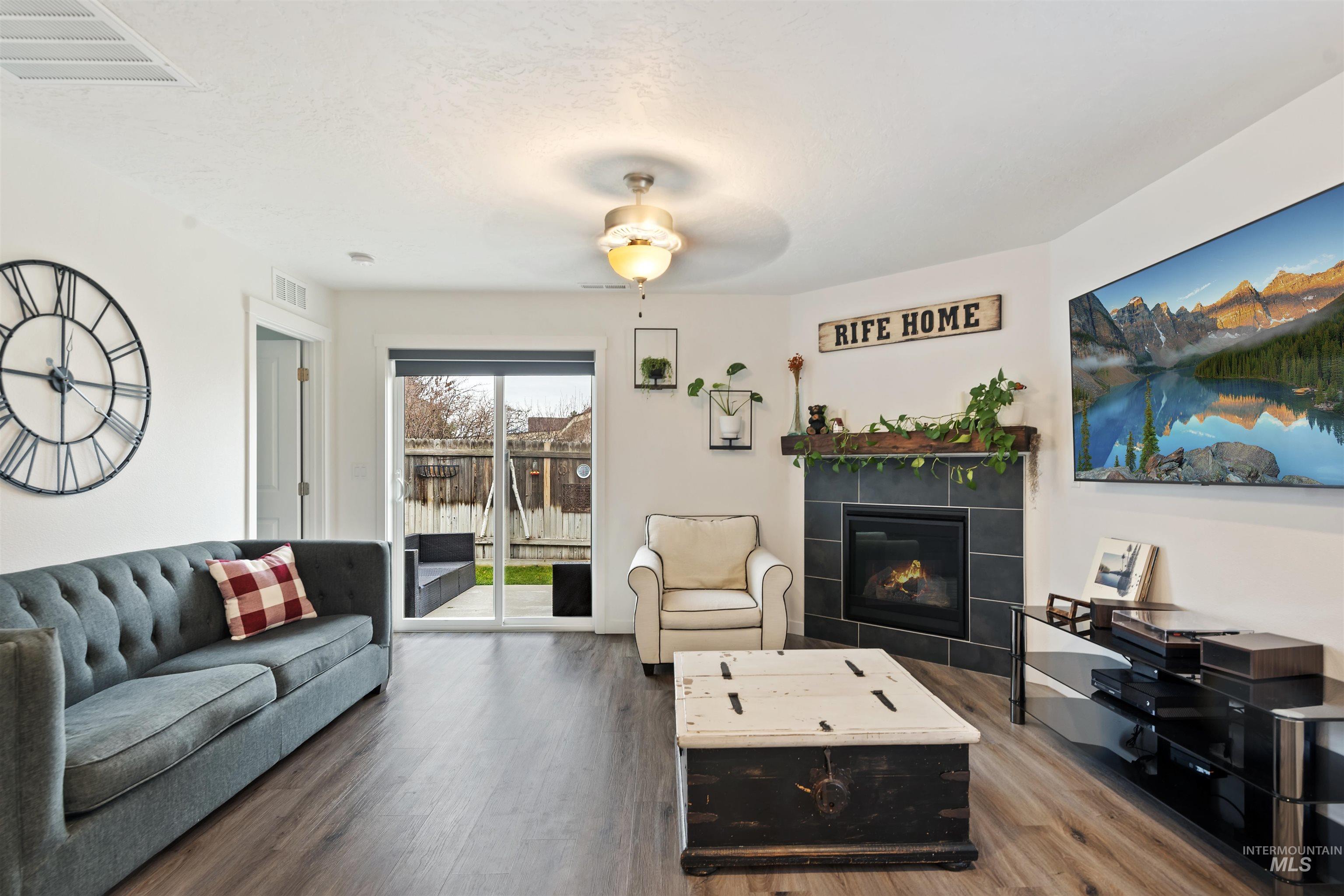 Living room featuring a tiled fireplace, a ceiling fan, and wood finished floors