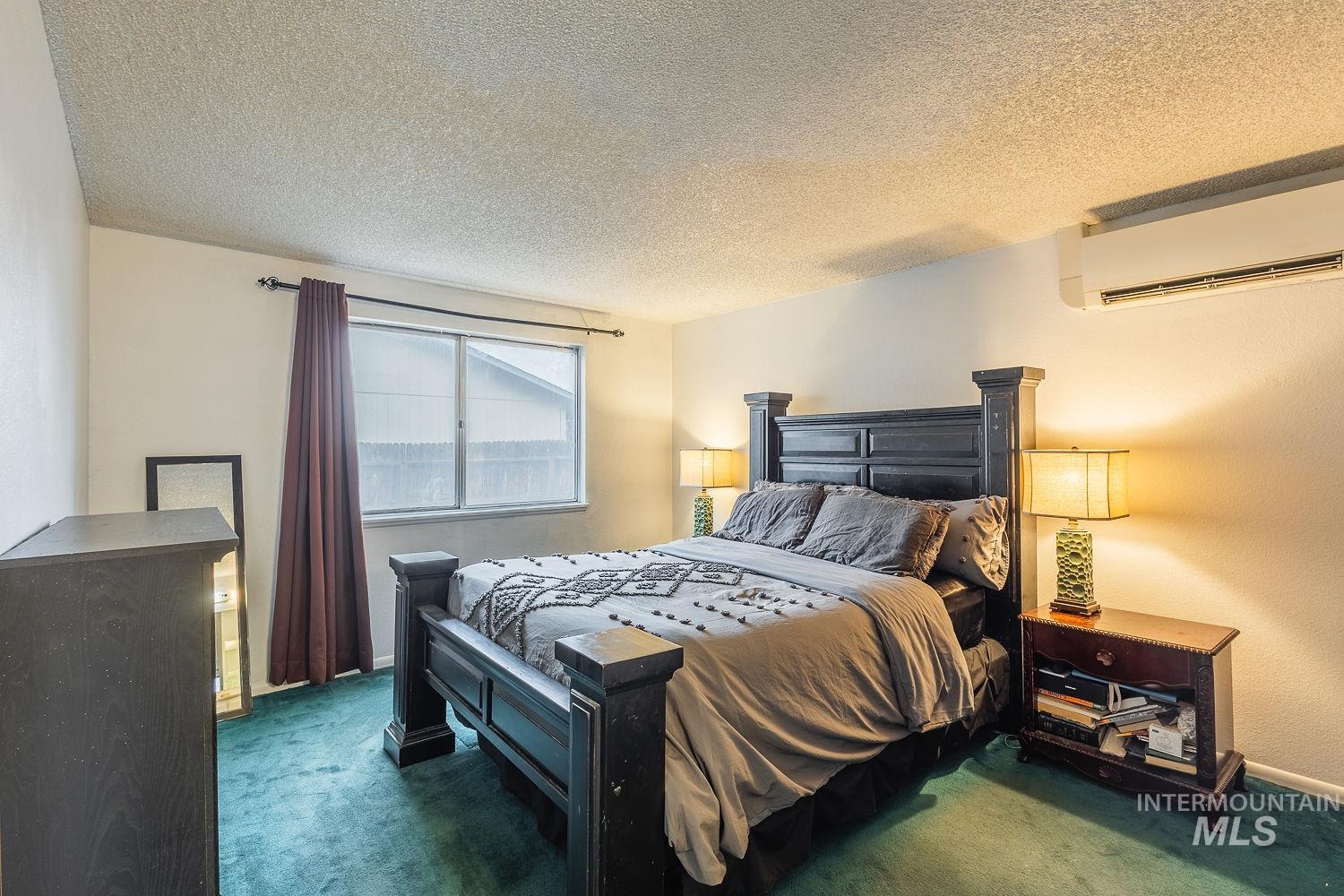 Carpeted bedroom with a textured ceiling and an AC wall unit
