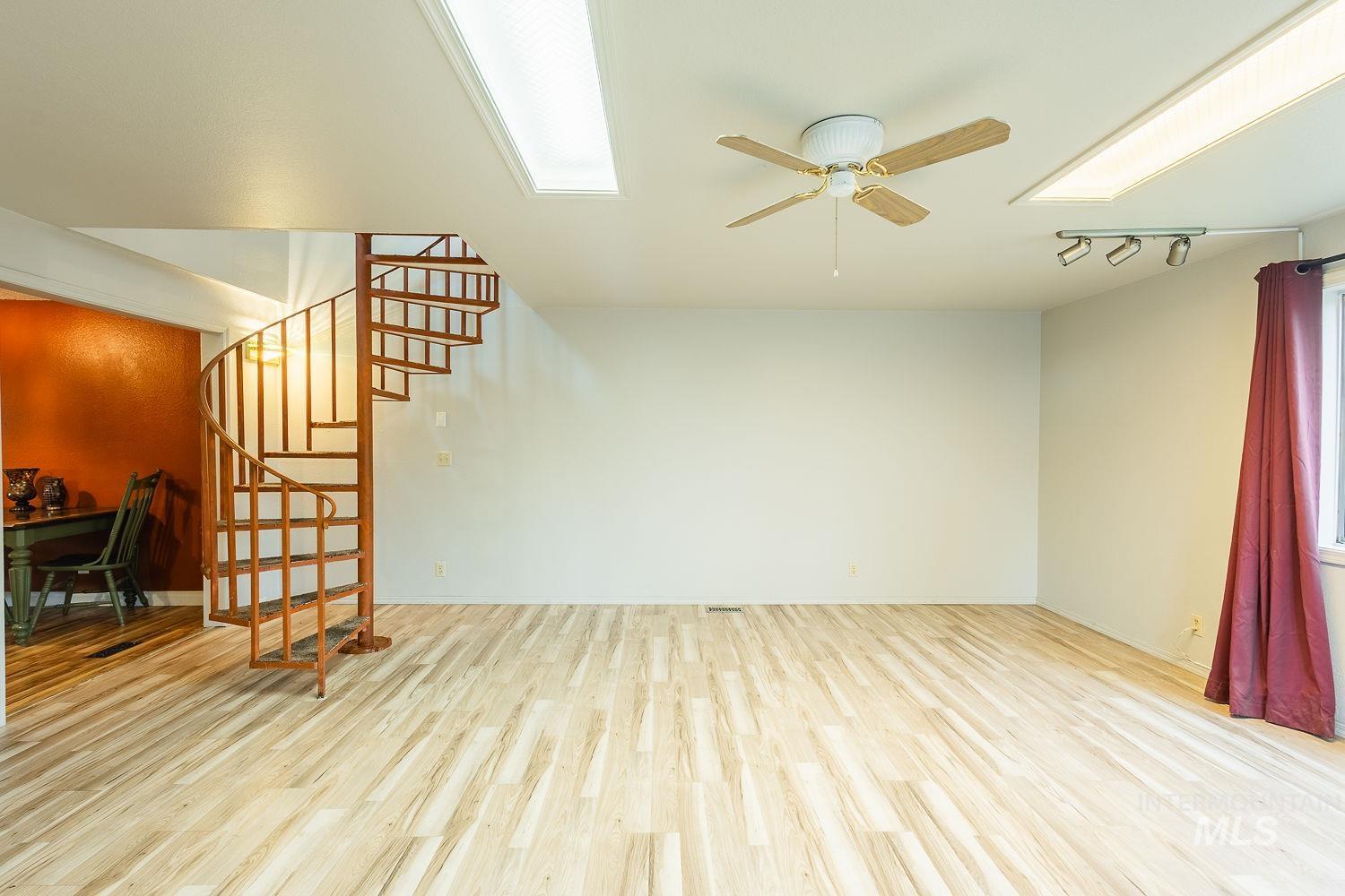 Unfurnished living room with light wood-style floors, stairs, a skylight, and ceiling fan