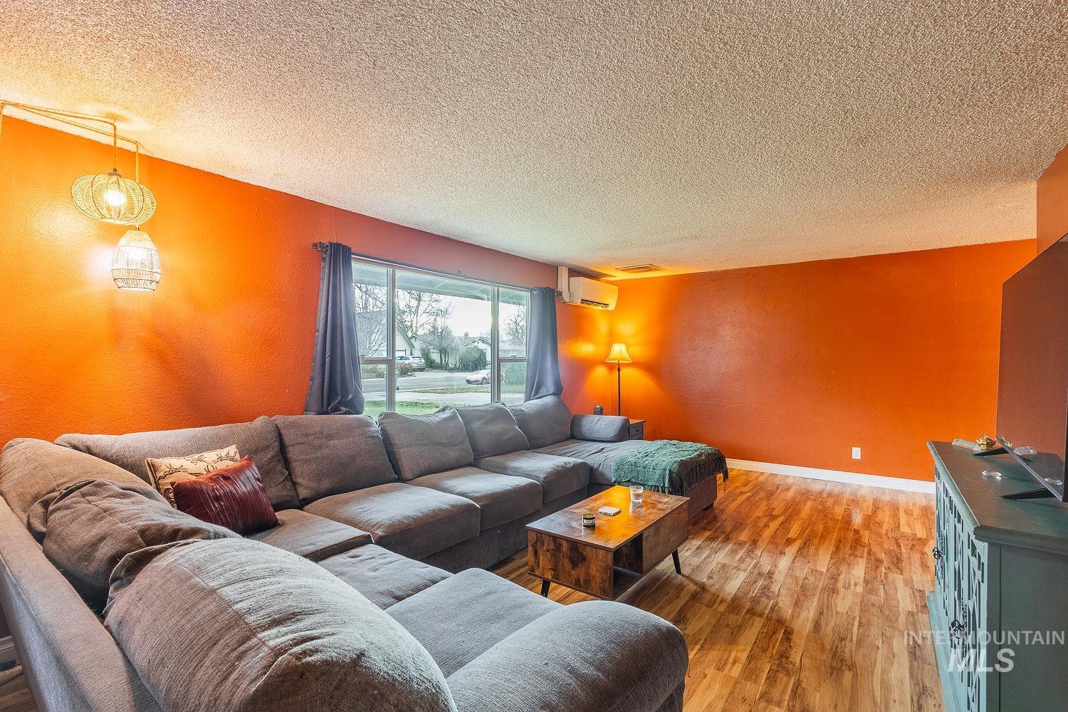 Living room featuring light wood-style floors, a textured ceiling, and a textured wall