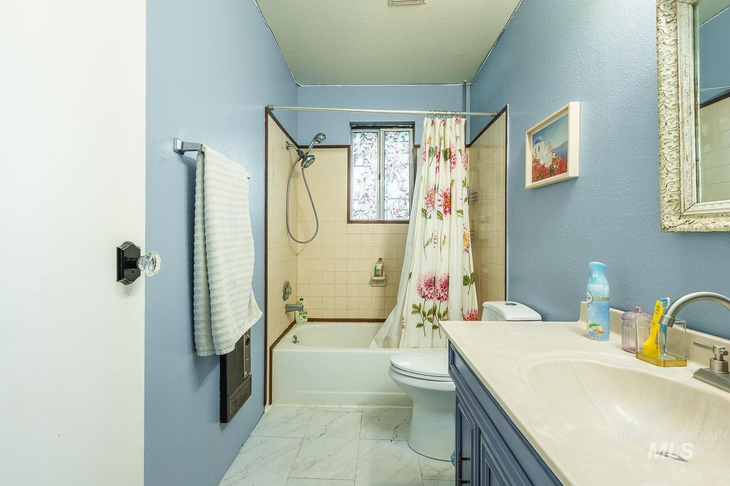 Bathroom featuring shower / tub combo with curtain, vanity, a textured wall, and light marble finish floors