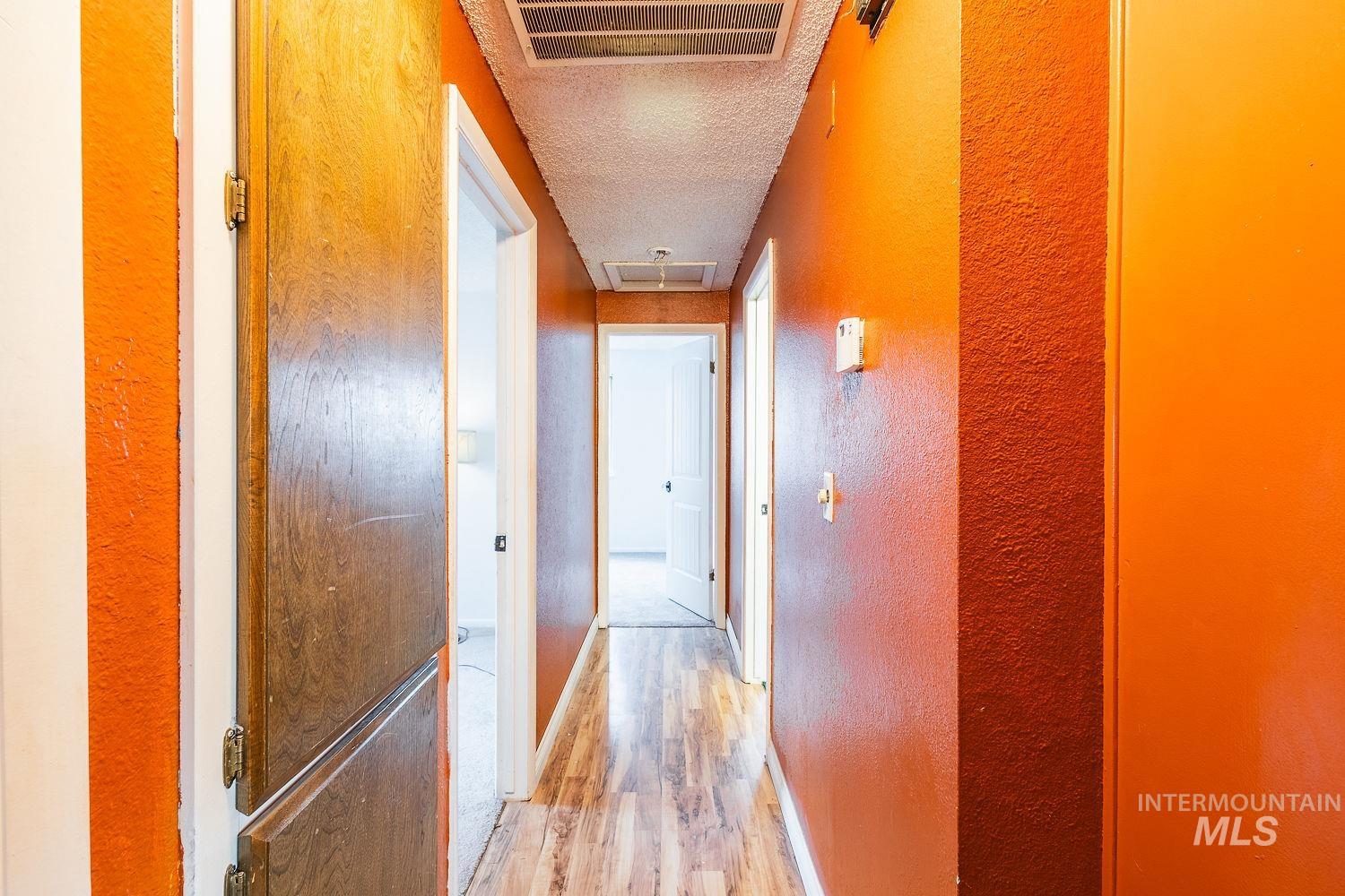 Hallway with a textured wall, a textured ceiling, and light wood-type flooring