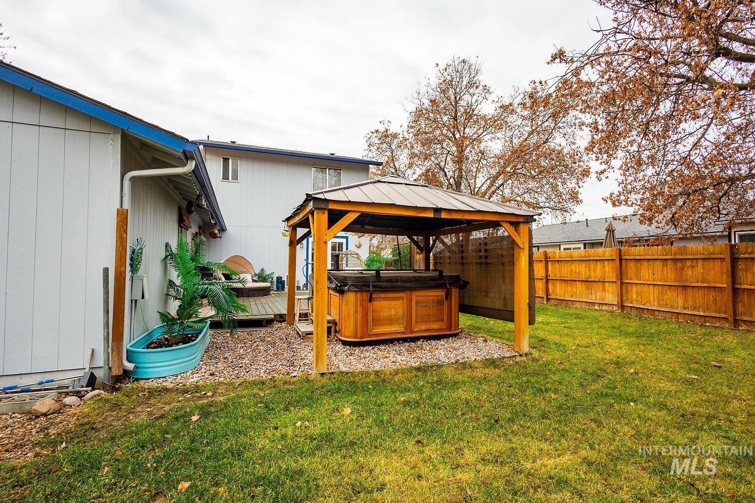 Fenced backyard featuring a hot tub, a gazebo, and a wooden deck