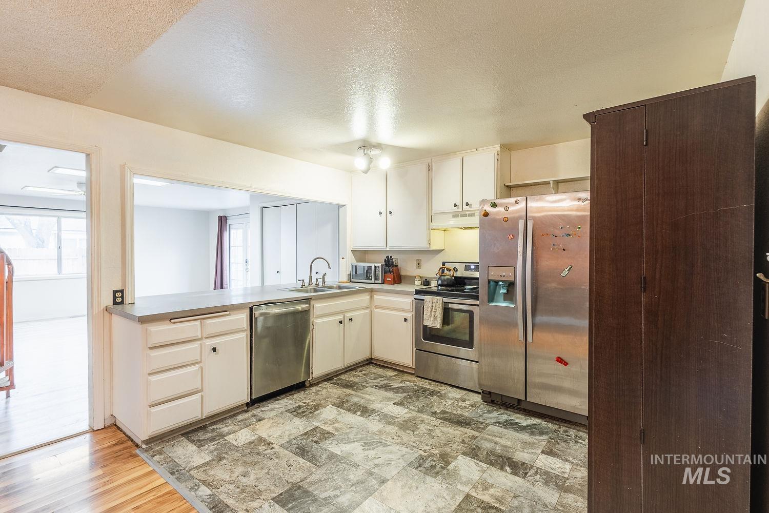 Kitchen with stainless steel appliances, a textured ceiling, light countertops, and under cabinet range hood