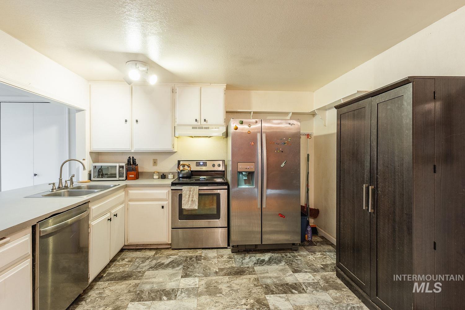 Kitchen with appliances with stainless steel finishes, light countertops, a textured ceiling, under cabinet range hood, and stone finish flooring