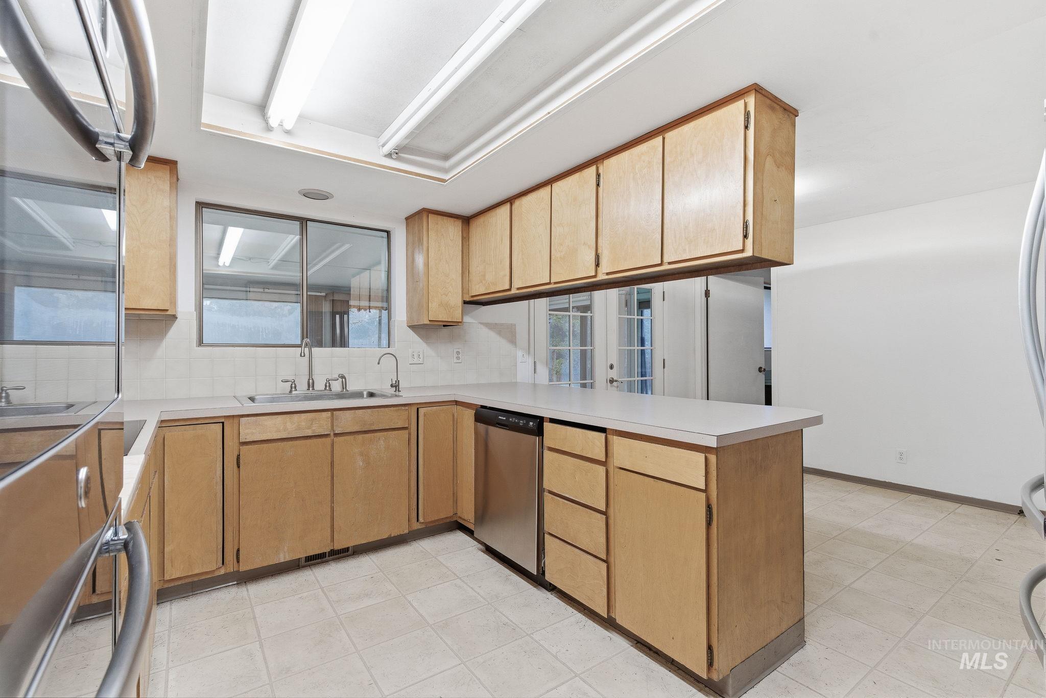 Kitchen featuring appliances with stainless steel finishes, light countertops, a peninsula, decorative backsplash, and light brown cabinetry
